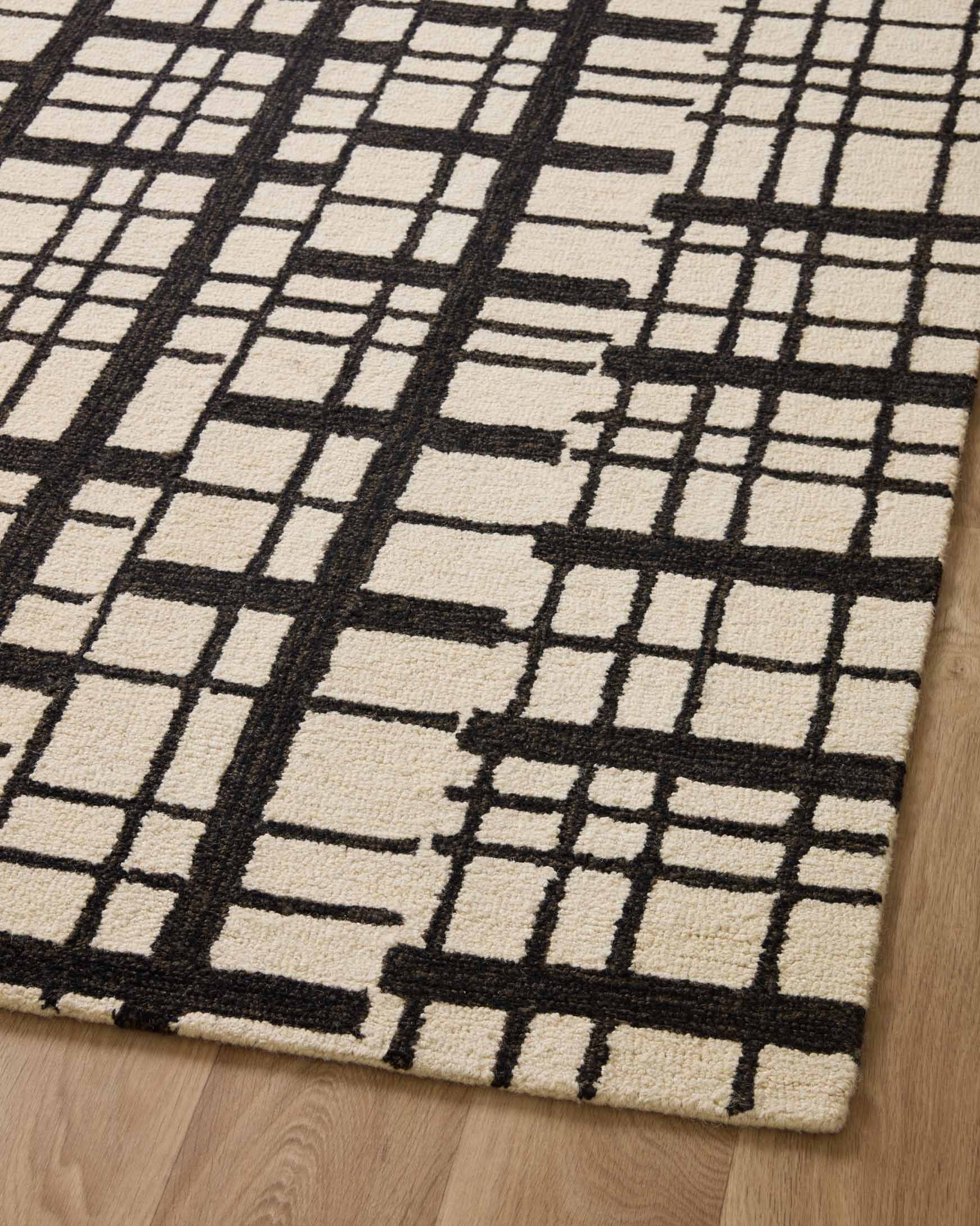 Overhead view of a black and ivory grid patchwork hand-tufted rug on wood floor.