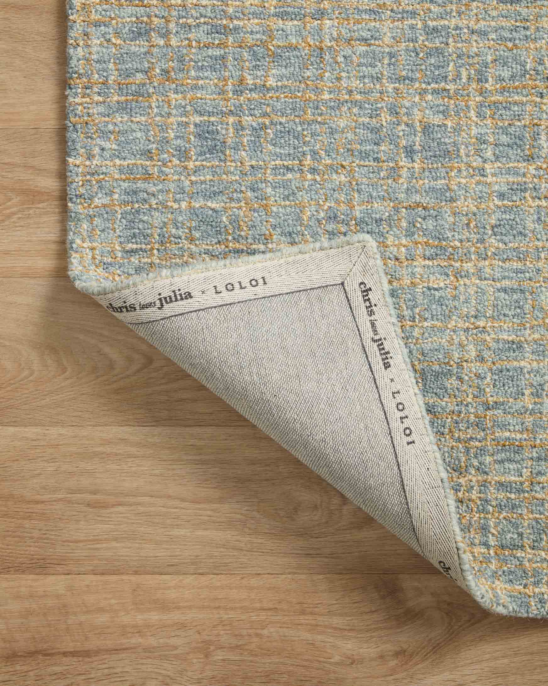 Rug corner showing woven label on the underside against the blue and sand surface.