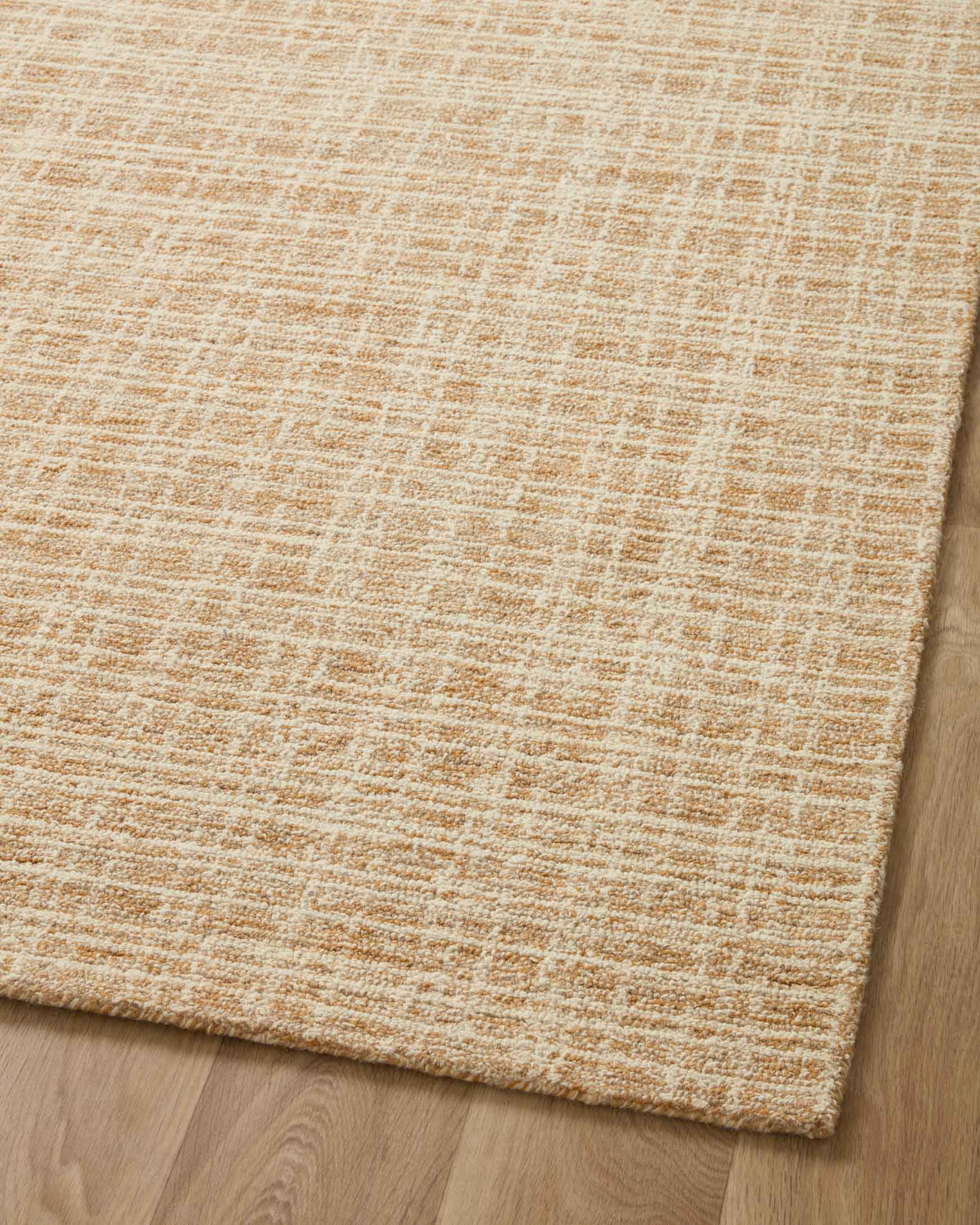 Straw-and-ivory hand-tufted area rug viewed from the edge on light wood flooring.