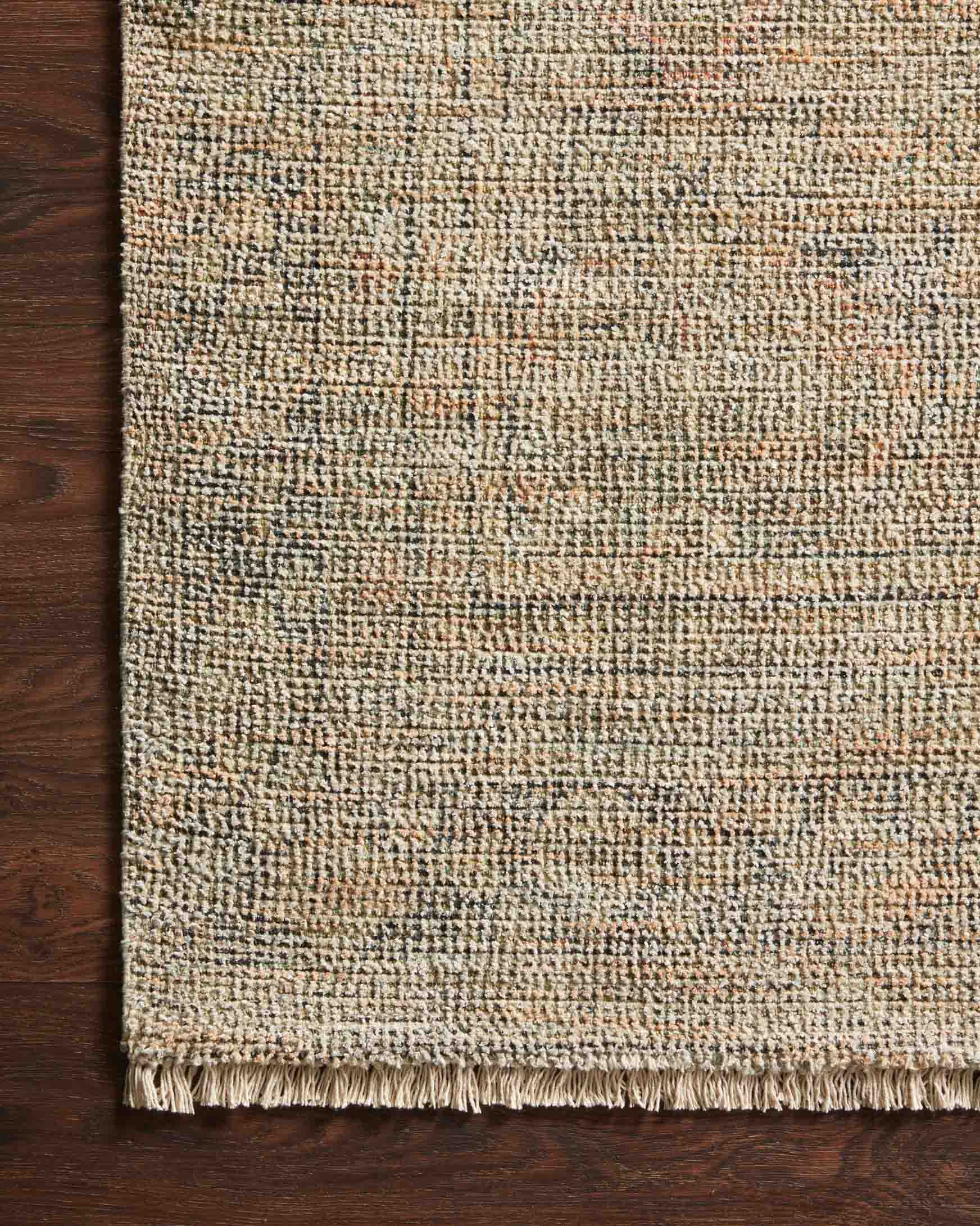 Hand-woven rug corner with fringe; textured tan surface with olive and gray specks.