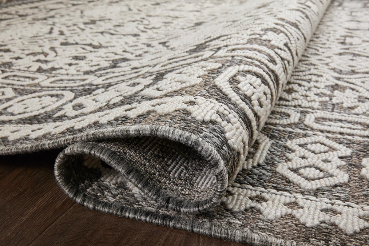 Close-up of pebble gray and ivory rug edge with stitched border and rolled texture