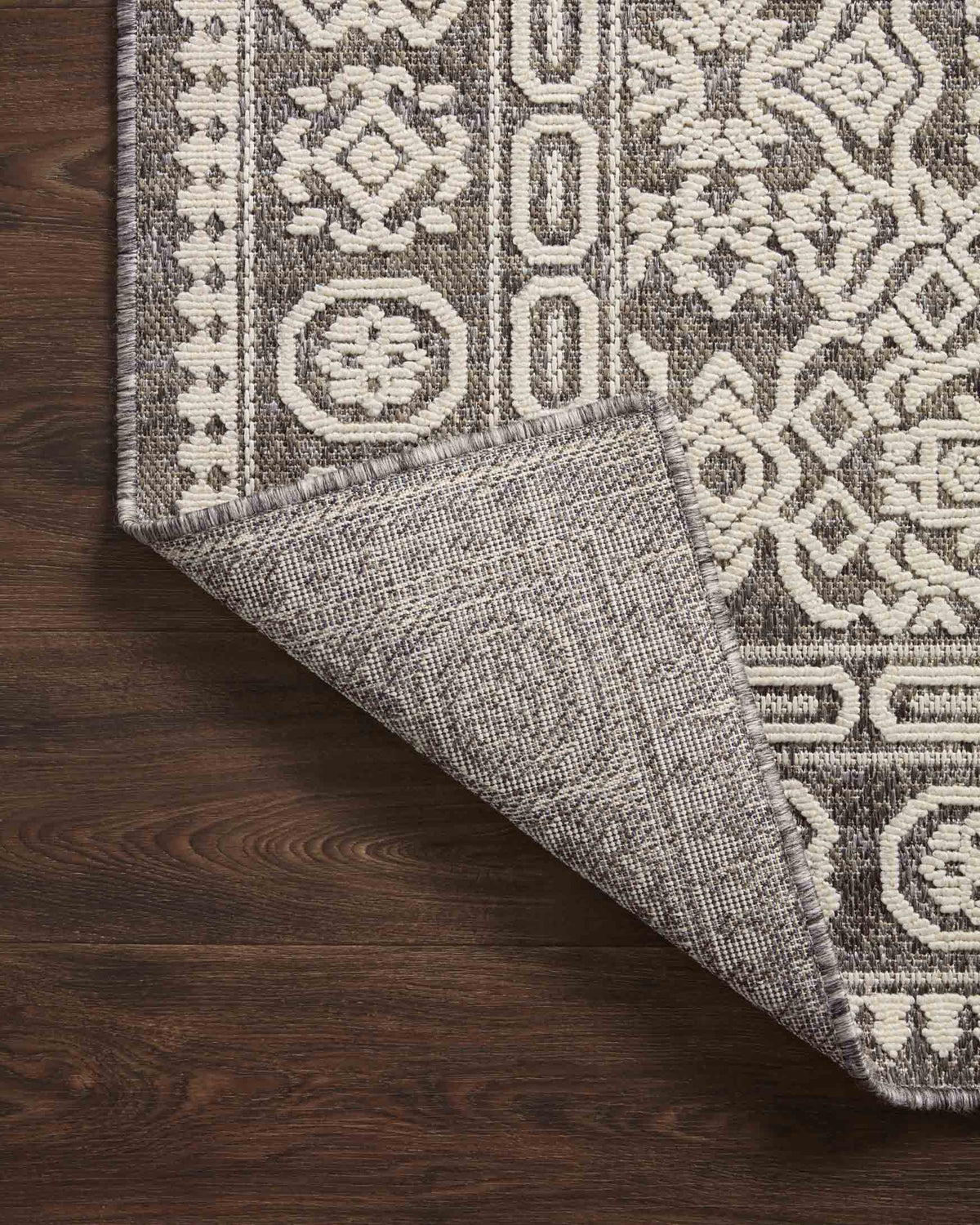 Corner drape of pebble gray and ivory geometric rug on dark wood flooring