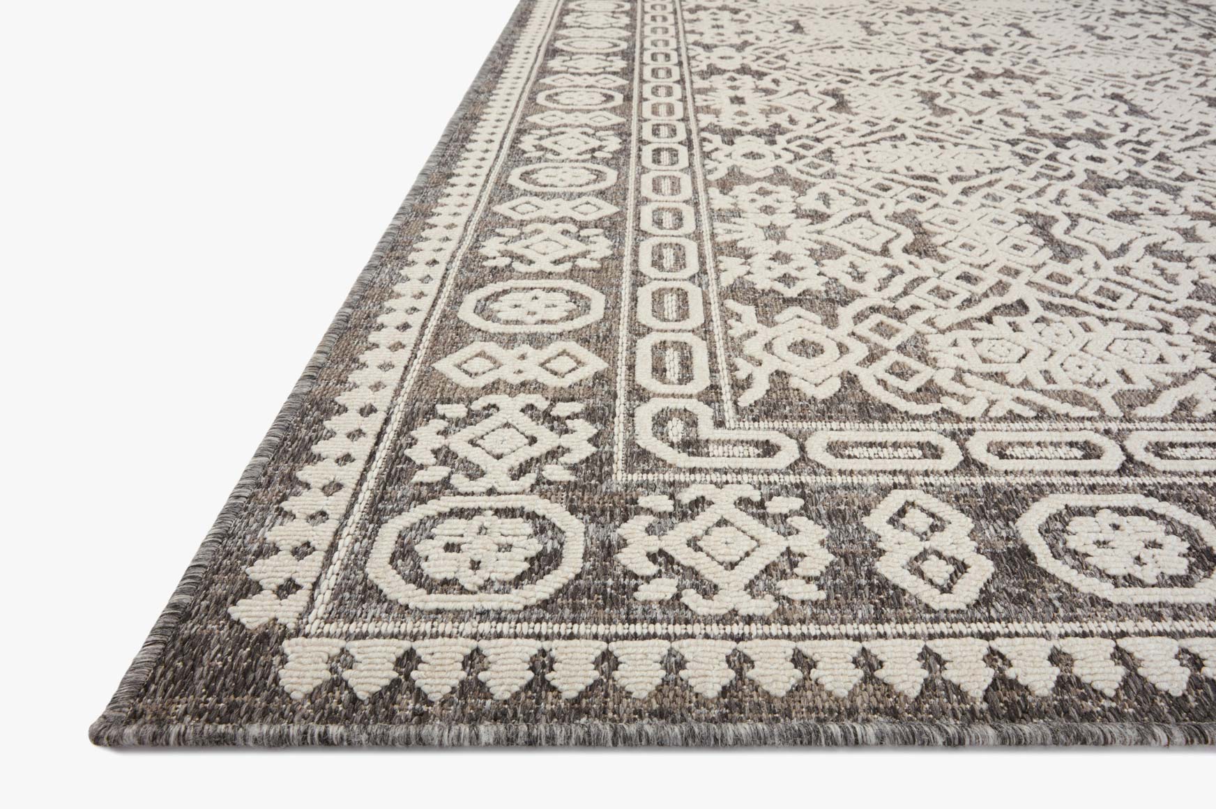 Corner view of pebble gray and ivory rug with ornate border and short tassel fringe