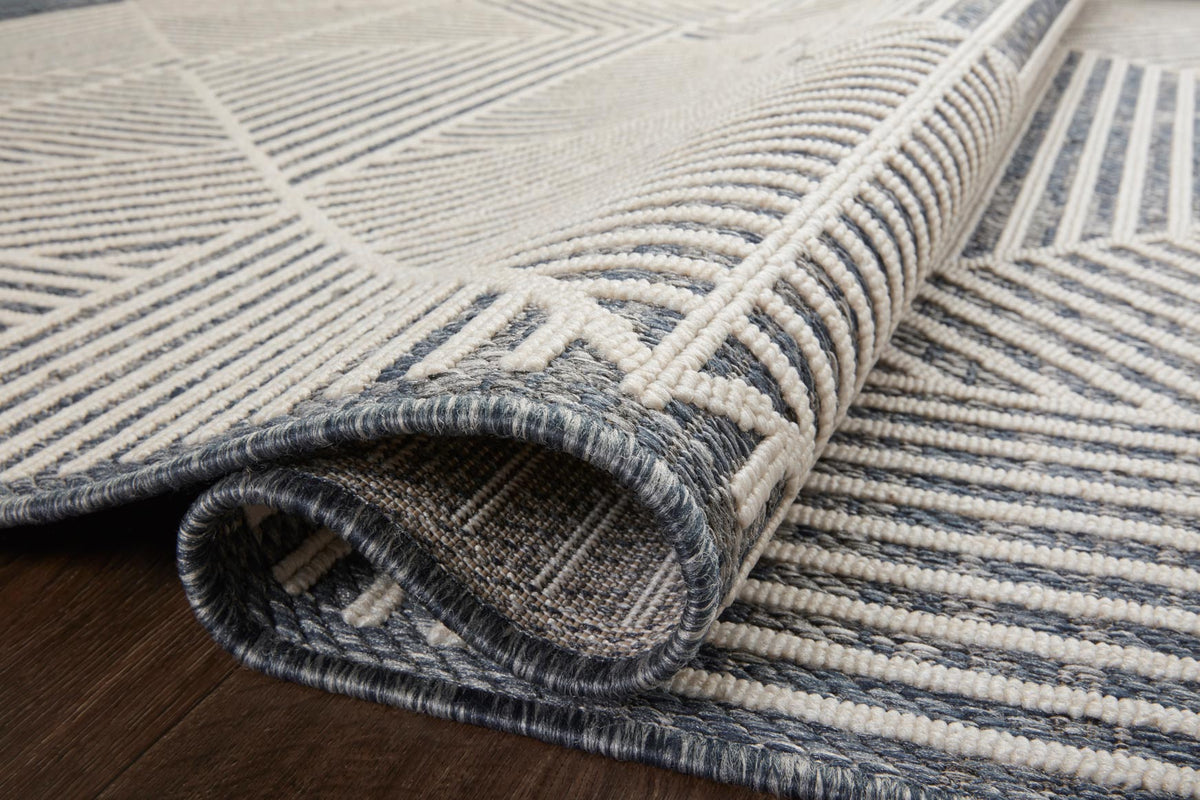 Denim and ivory geometric rug edge with stitched border and rolled underside