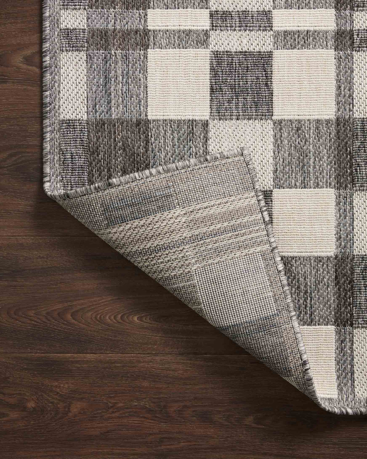 Corner of ivory and pebble checkered rug with stitched border, laid on dark wood