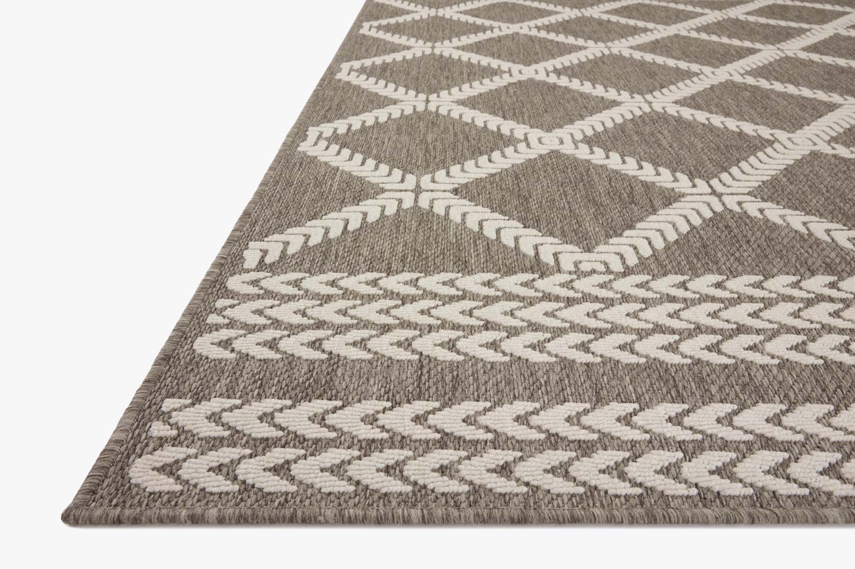 Indoor/outdoor rug corner view with dark gray and ivory diamond and zigzag motifs