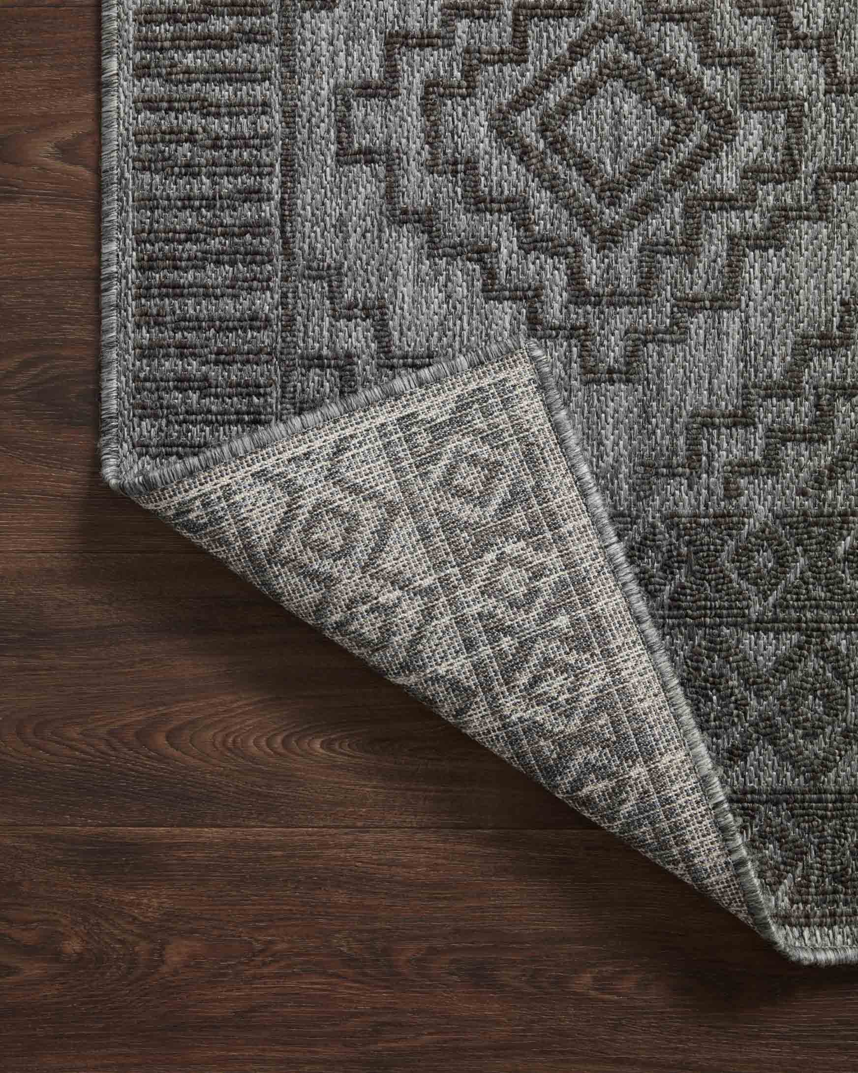 Grey and charcoal rug corner folded to show reverse weave texture and geometric motif.