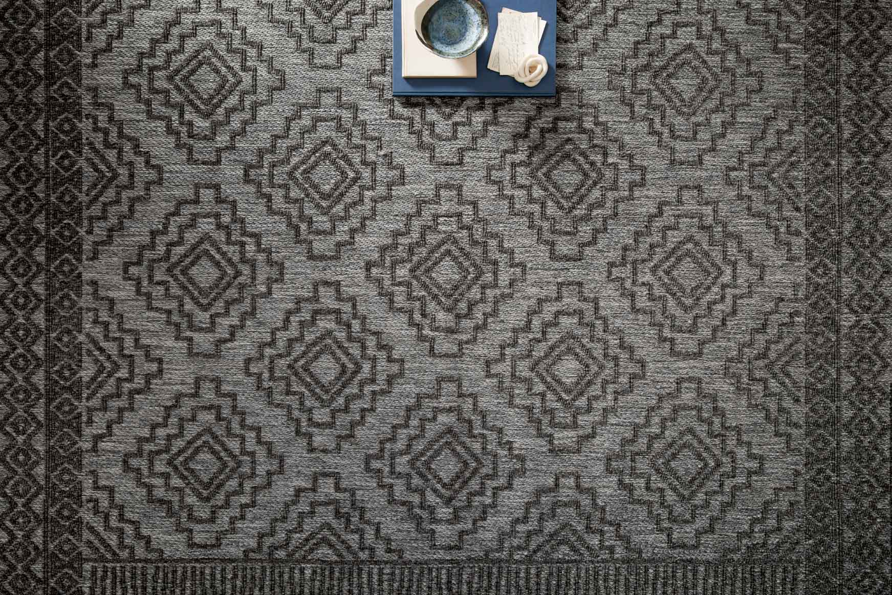 Grey and charcoal rug close-up showing repeating diamond and zigzag geometric pattern.