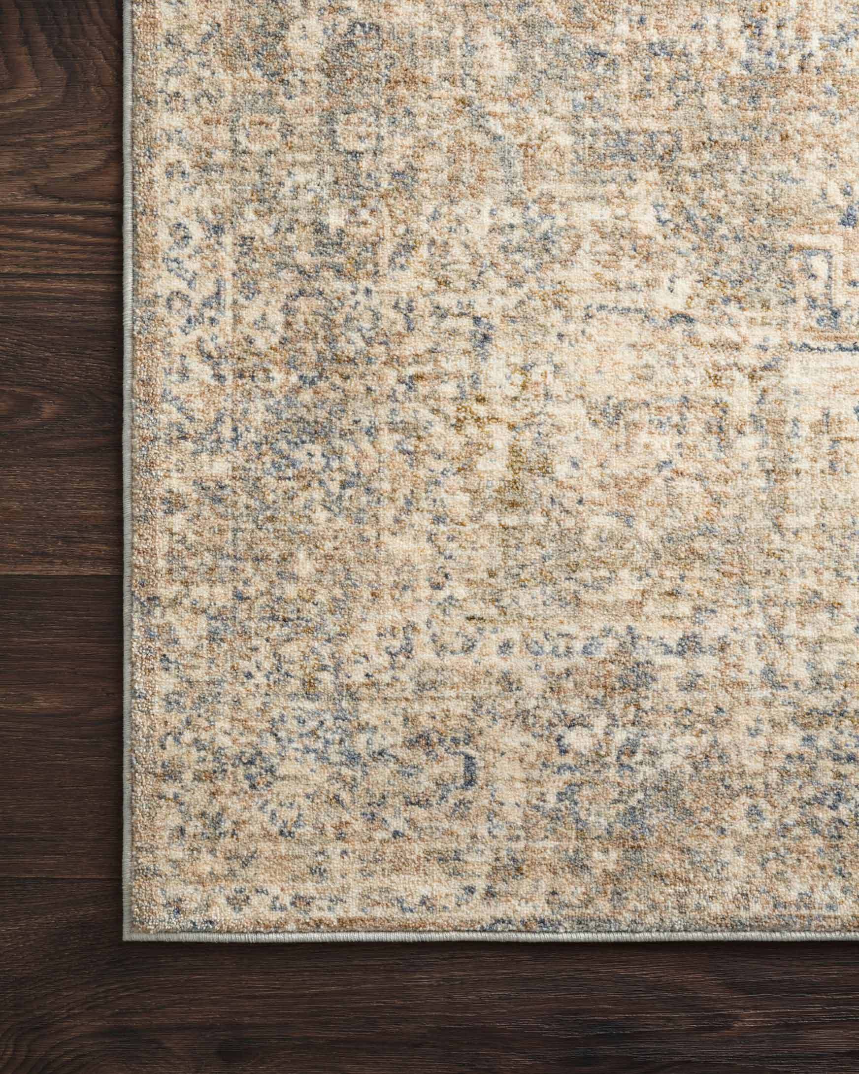 Traditional power-loomed rug corner on dark wood floor, beige and blue distressed pattern