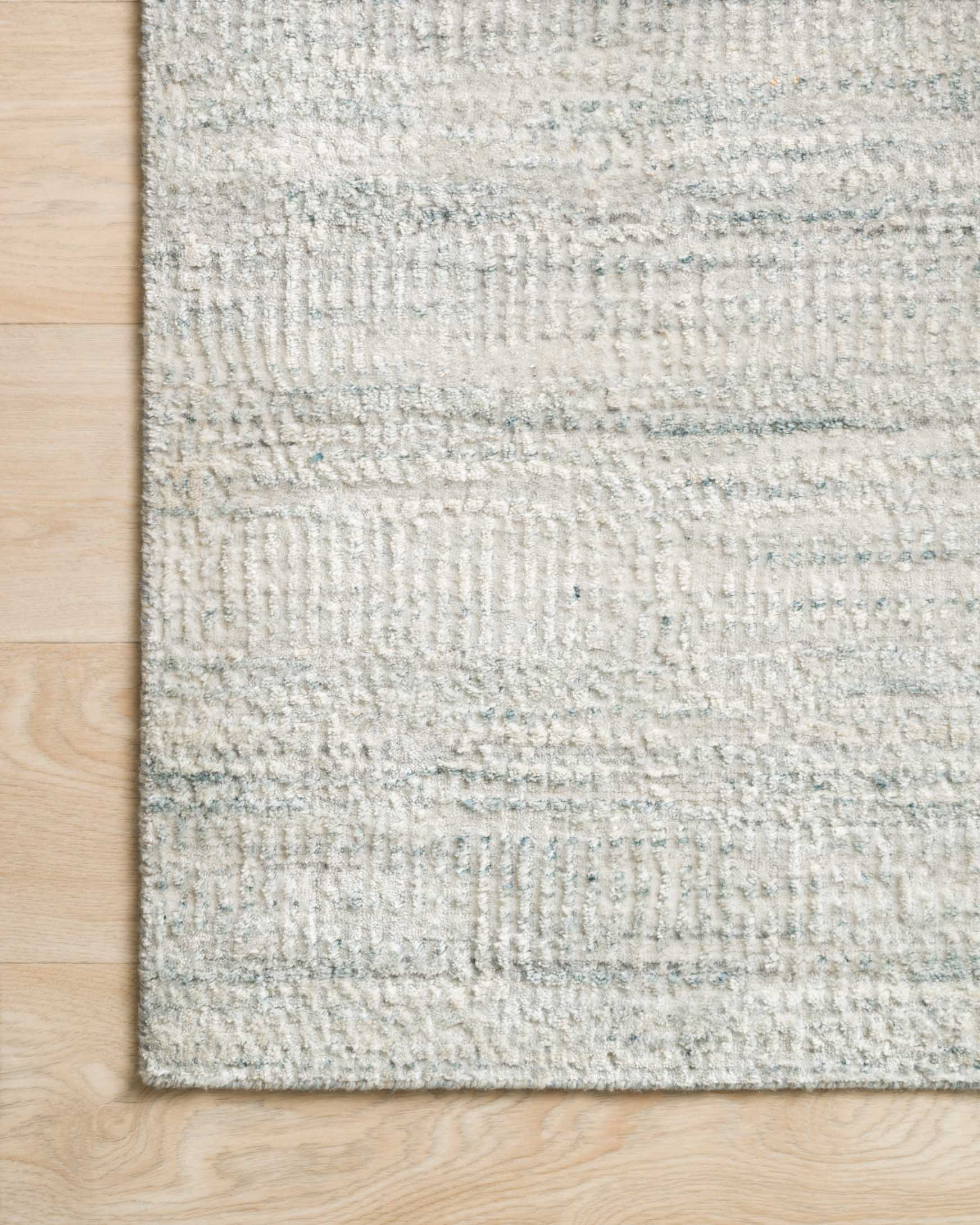Silver-gray hand-loomed rug corner detail with textured flat weave and thin stripes.