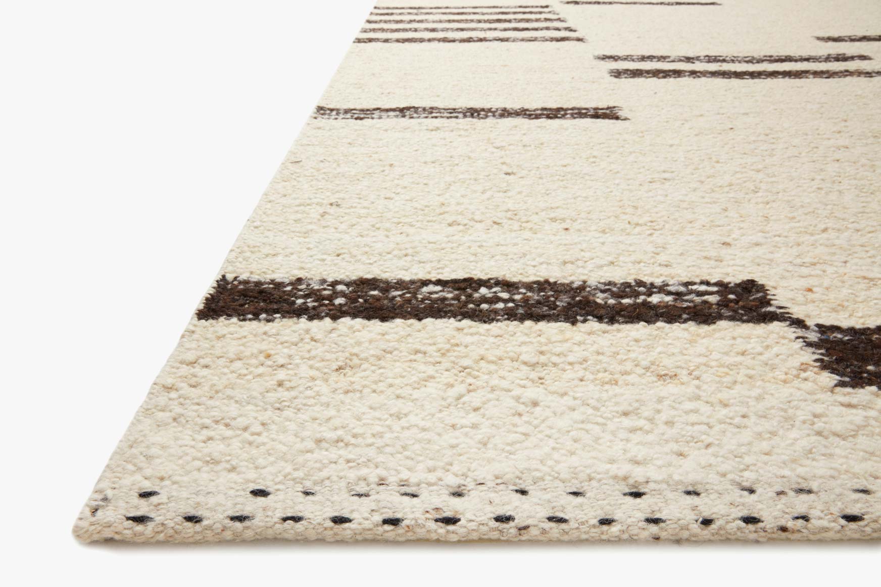 Corner of natural hand-woven rug showing dark stripe border and stitched edge