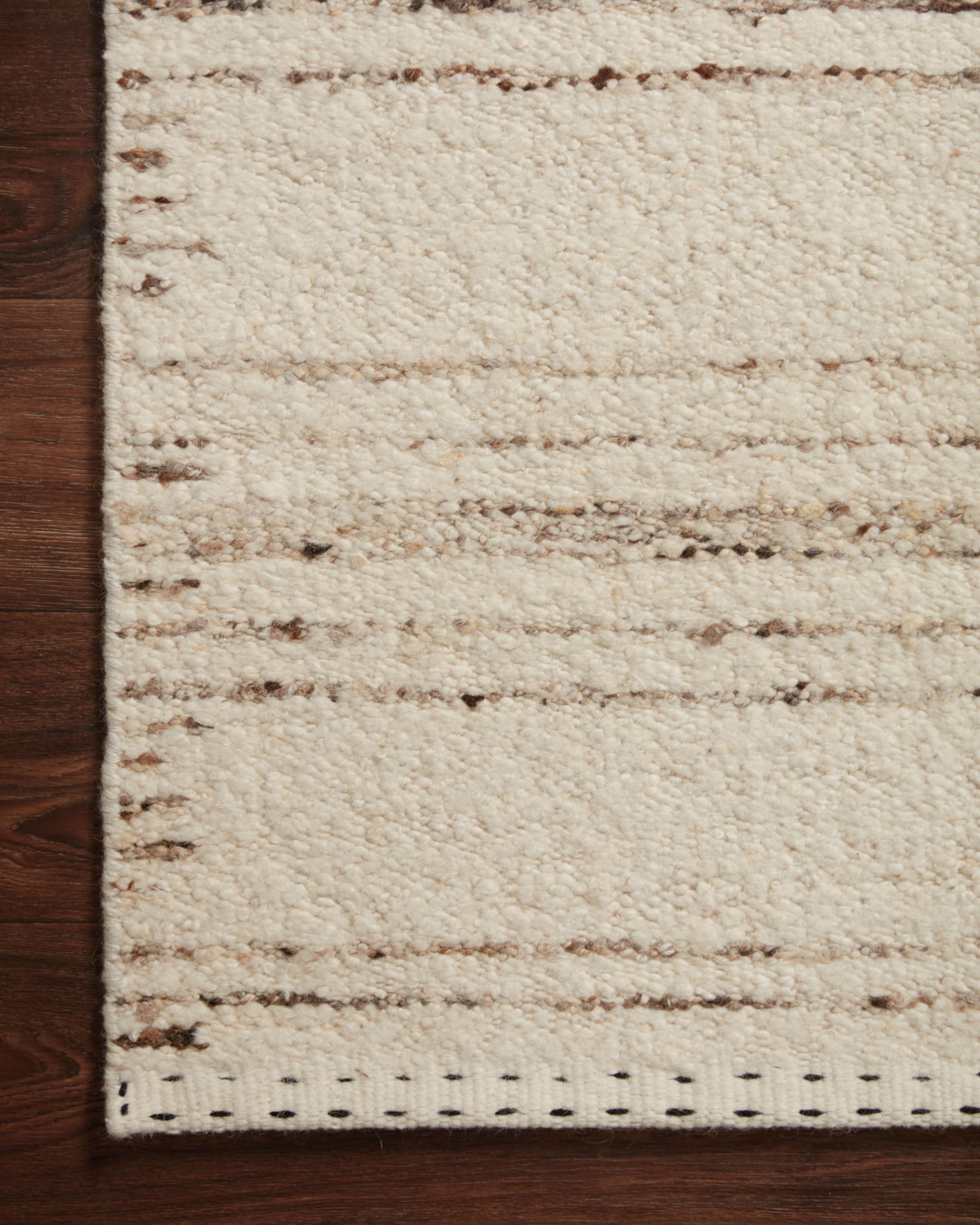 Close-up of ivory and pebble rug showing textured loops, horizontal bands, and stitched edge