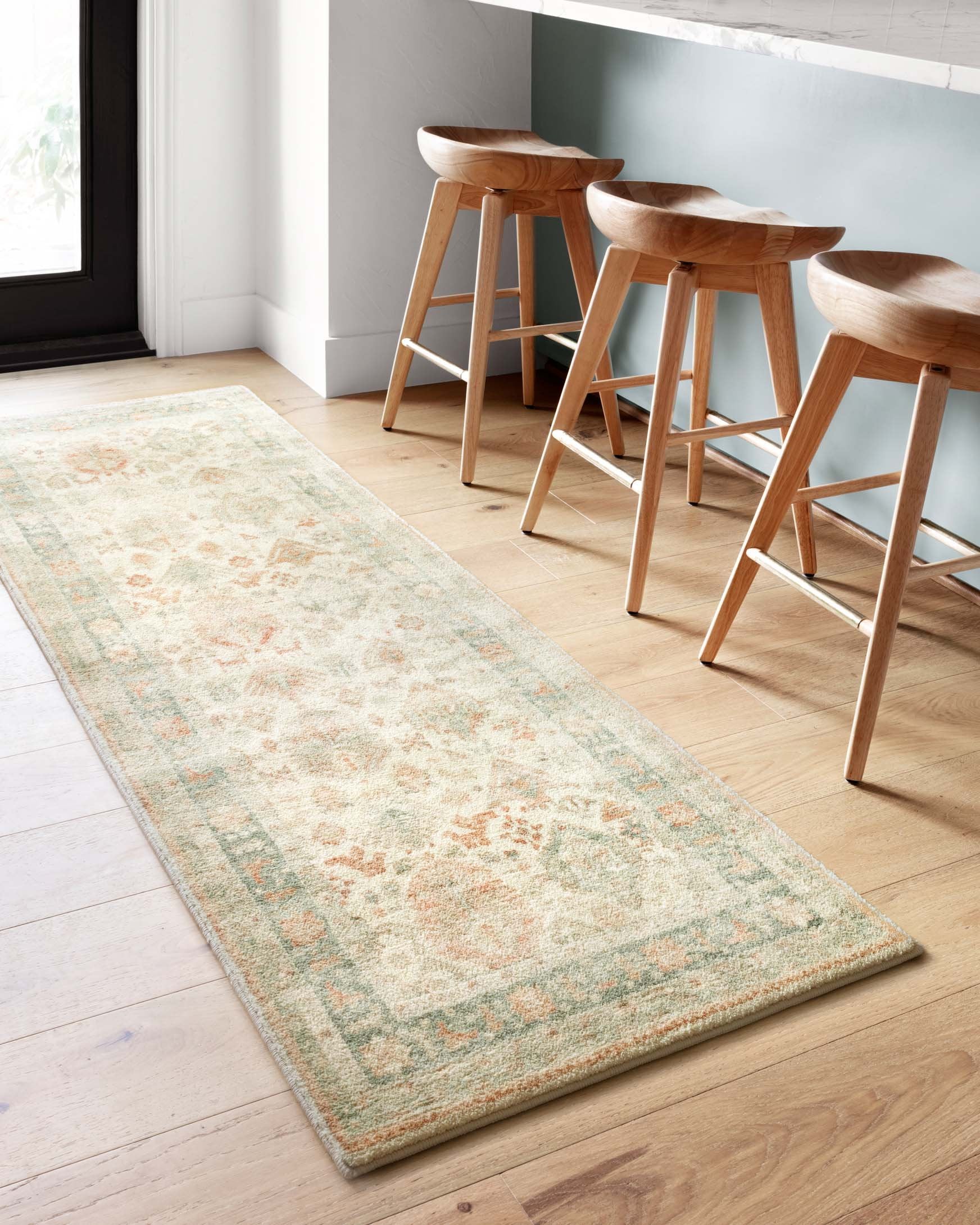 Beige area rug with wide border and faded motif pattern on light wood flooring