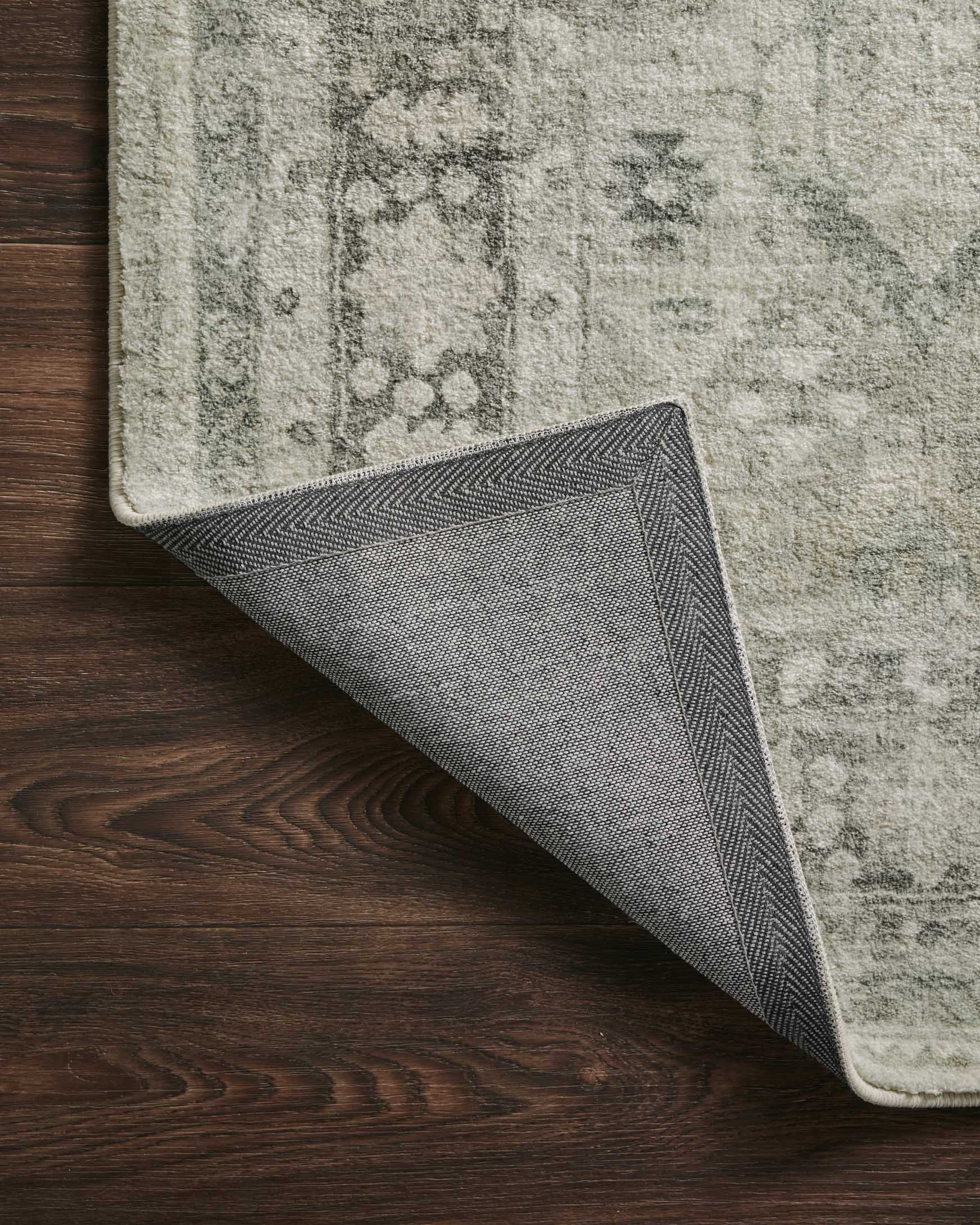 Steel-gray rug corner with reverse side visible and diagonal edge seam detail