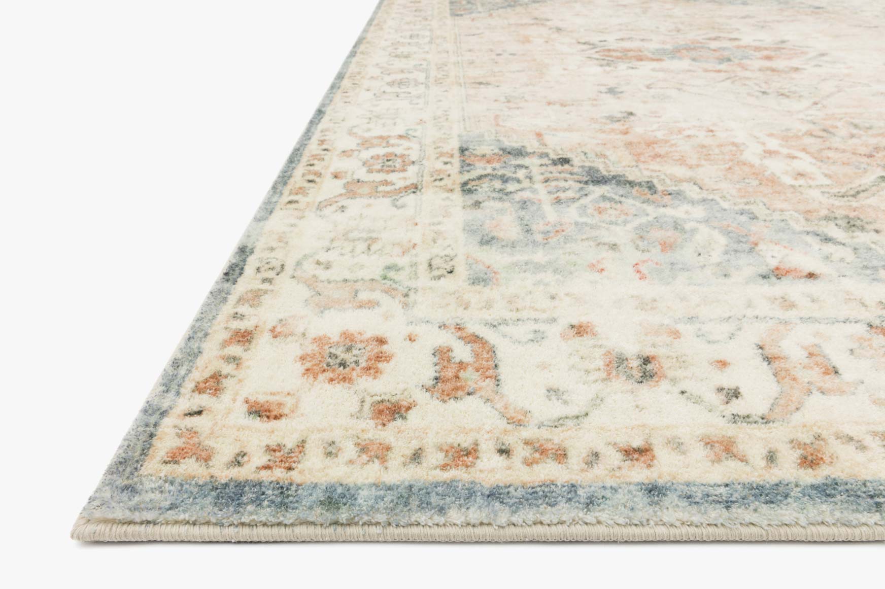 Close-up of ivory rug with faded floral and geometric motifs, teal-blue border trim