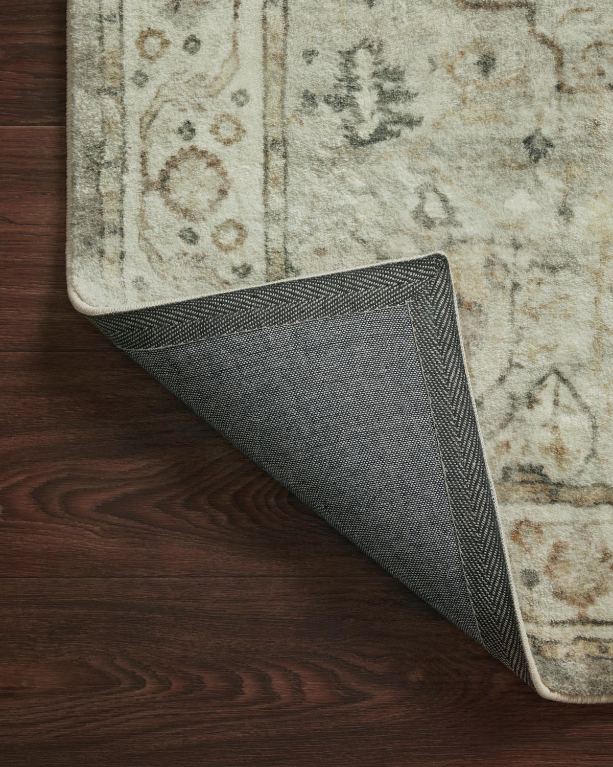 Rug corner lifted to show woven dark backing and light stitched edge binding.