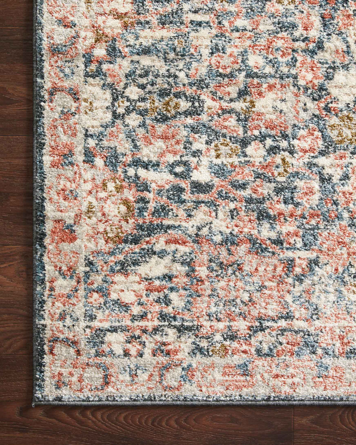 Corner detail of distressed area rug with floral pattern in navy, rust, and cream