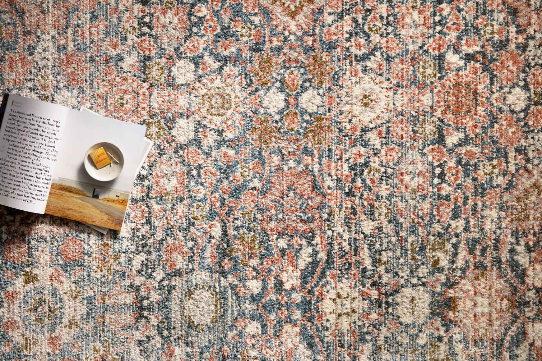 Close-up of distressed rug pattern with small floral motifs in navy, rust, and cream