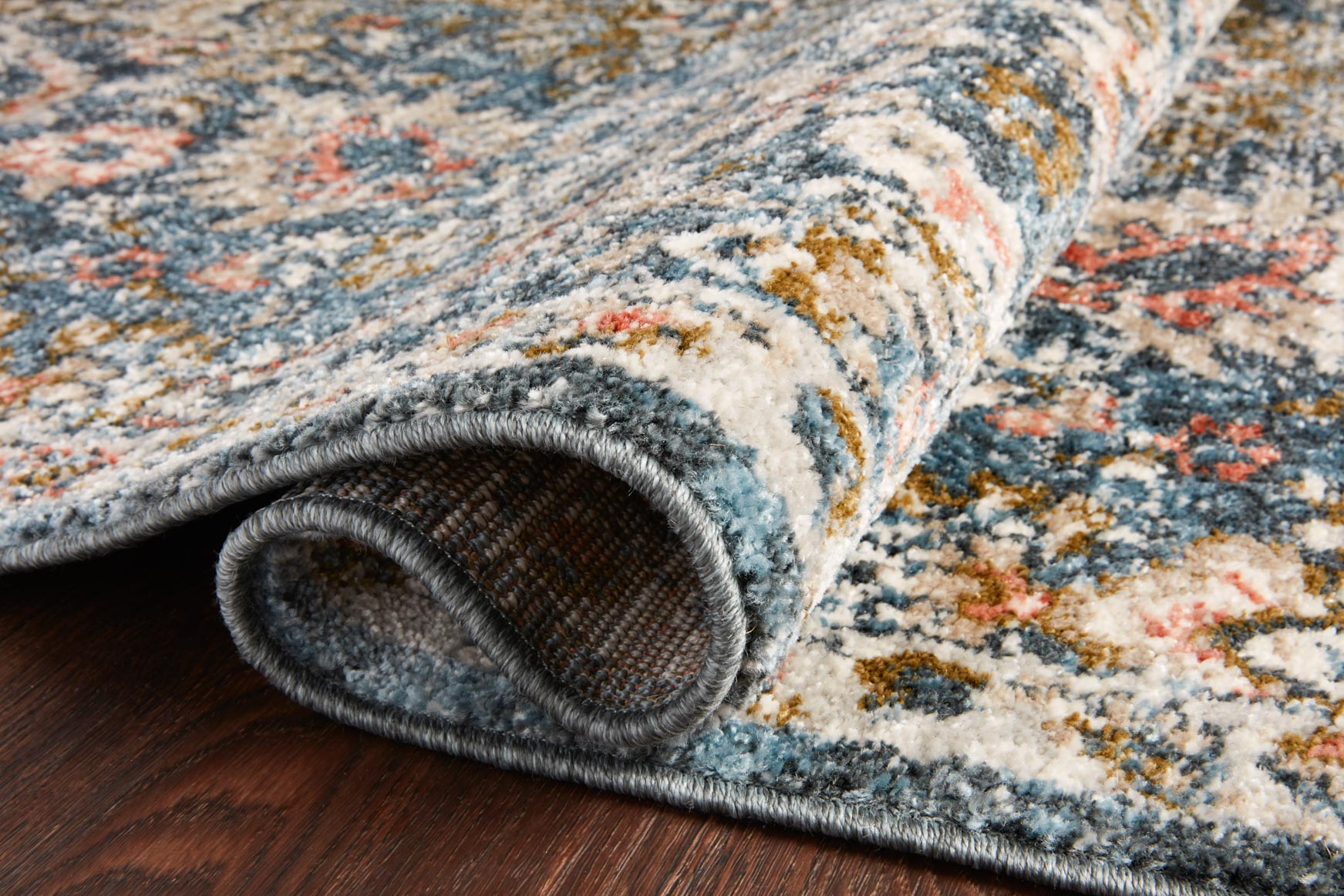 Rolled edge of blue and sand traditional rug with short pile and ornate motif design.