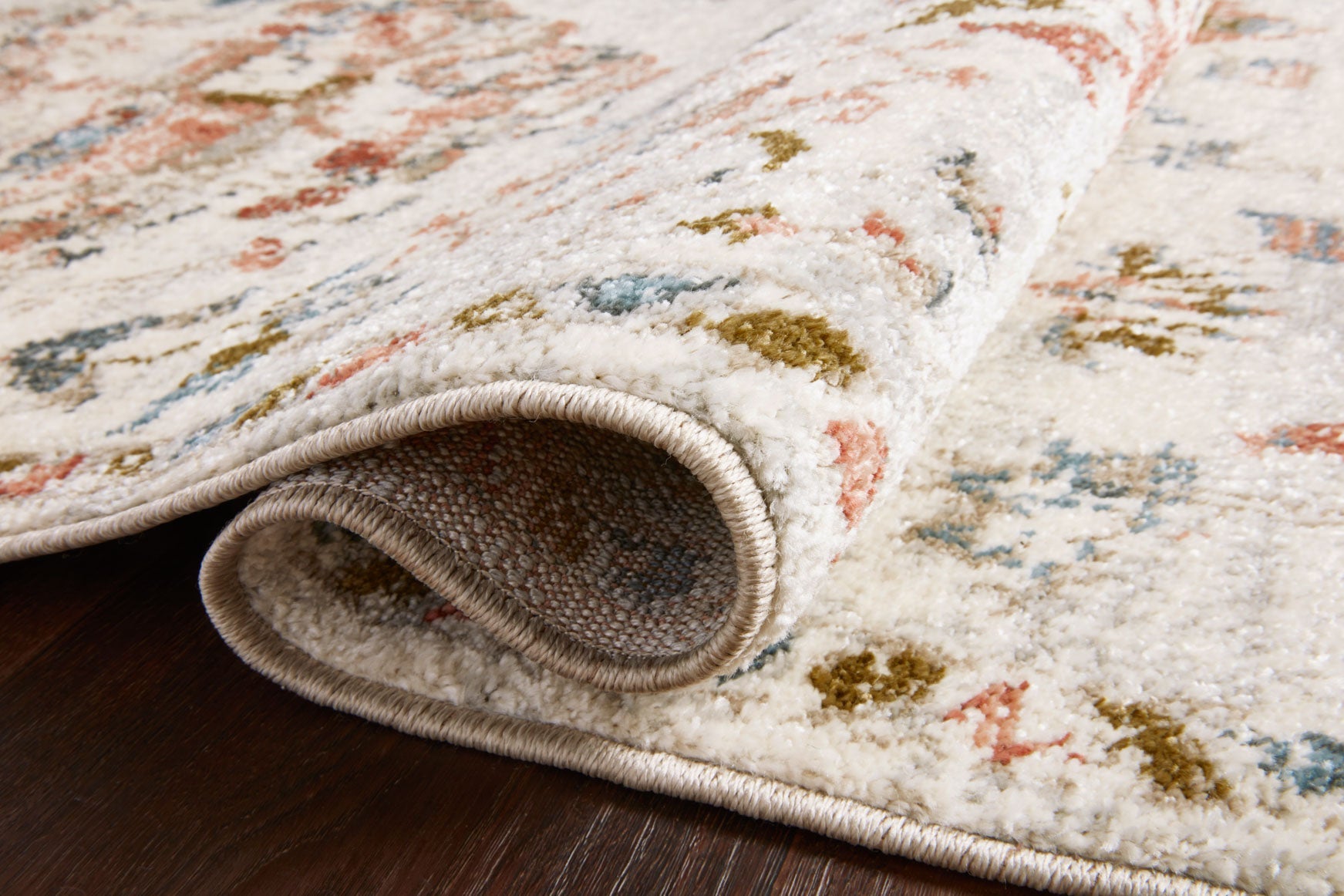 Close-up of ivory rug pile with multicolor speckled motifs and stitched edge