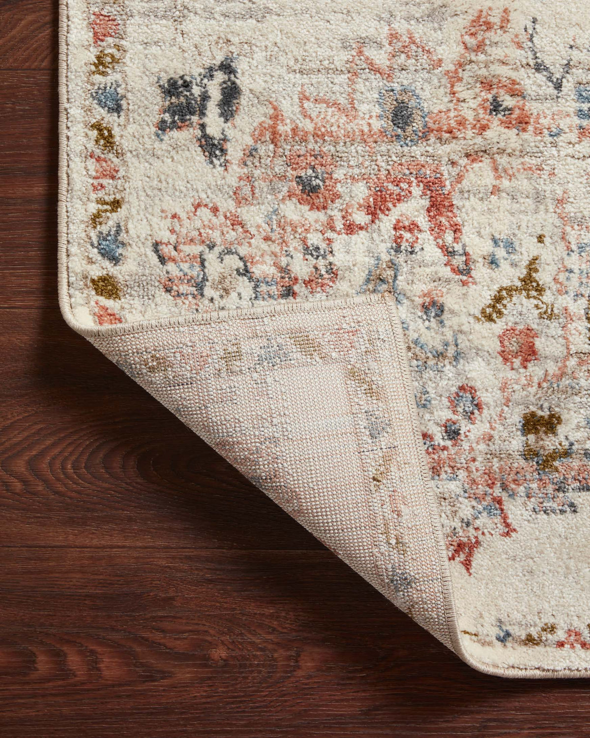 Ivory rug corner showing underside weave with multicolor motifs and binding