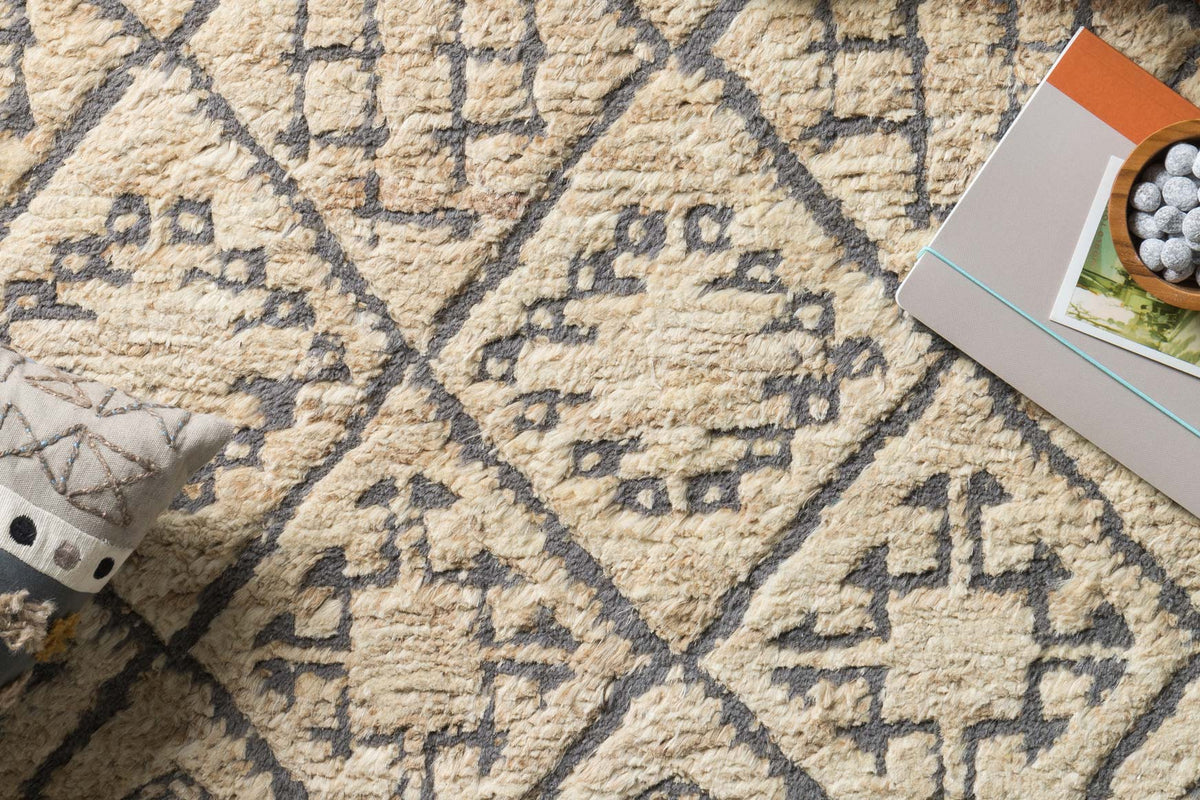 Close-up of hand-knotted rug texture with tan loops and dark blue geometric pattern.
