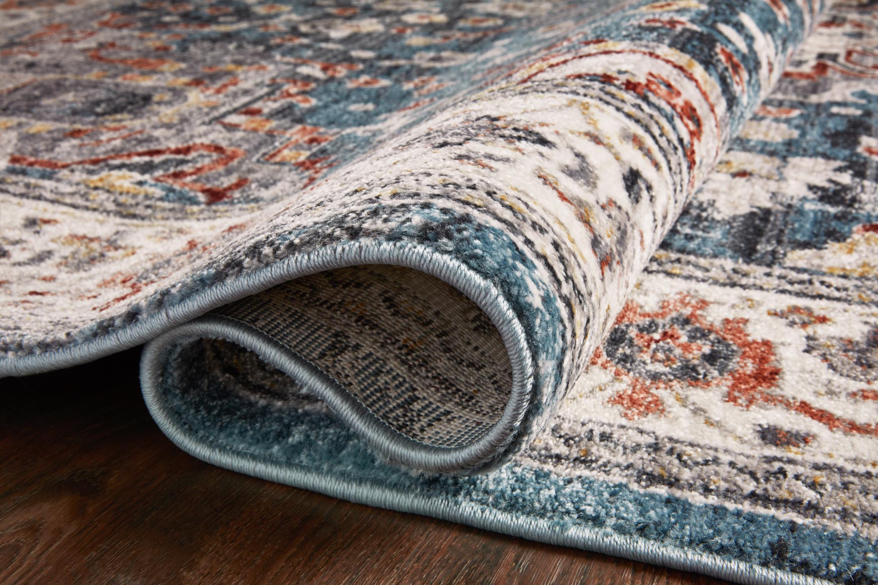 Power-loomed rug corner showing thick pile and tonal fringe trim in slate-blue and cream
