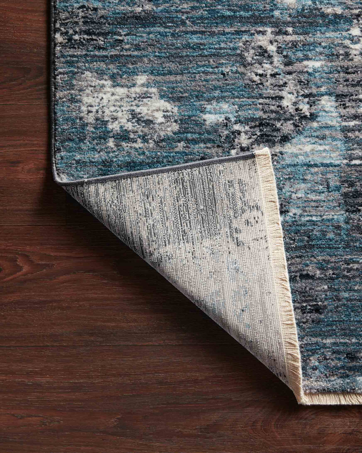 Corner with exposed backing and binding on blue-and-dove distressed rug.