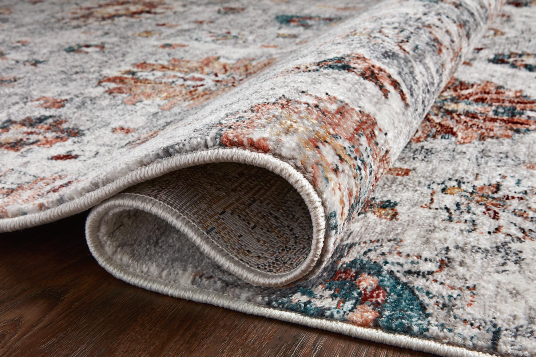 Ivory rug edge detail with braided border, short fringe, and multicolor motif background.