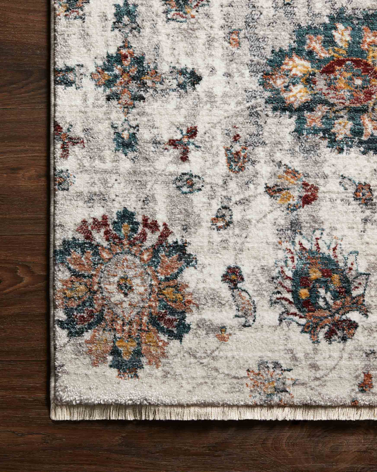 Ivory rug close-up on dark wood floor, showing teal and orange floral medallion pattern.