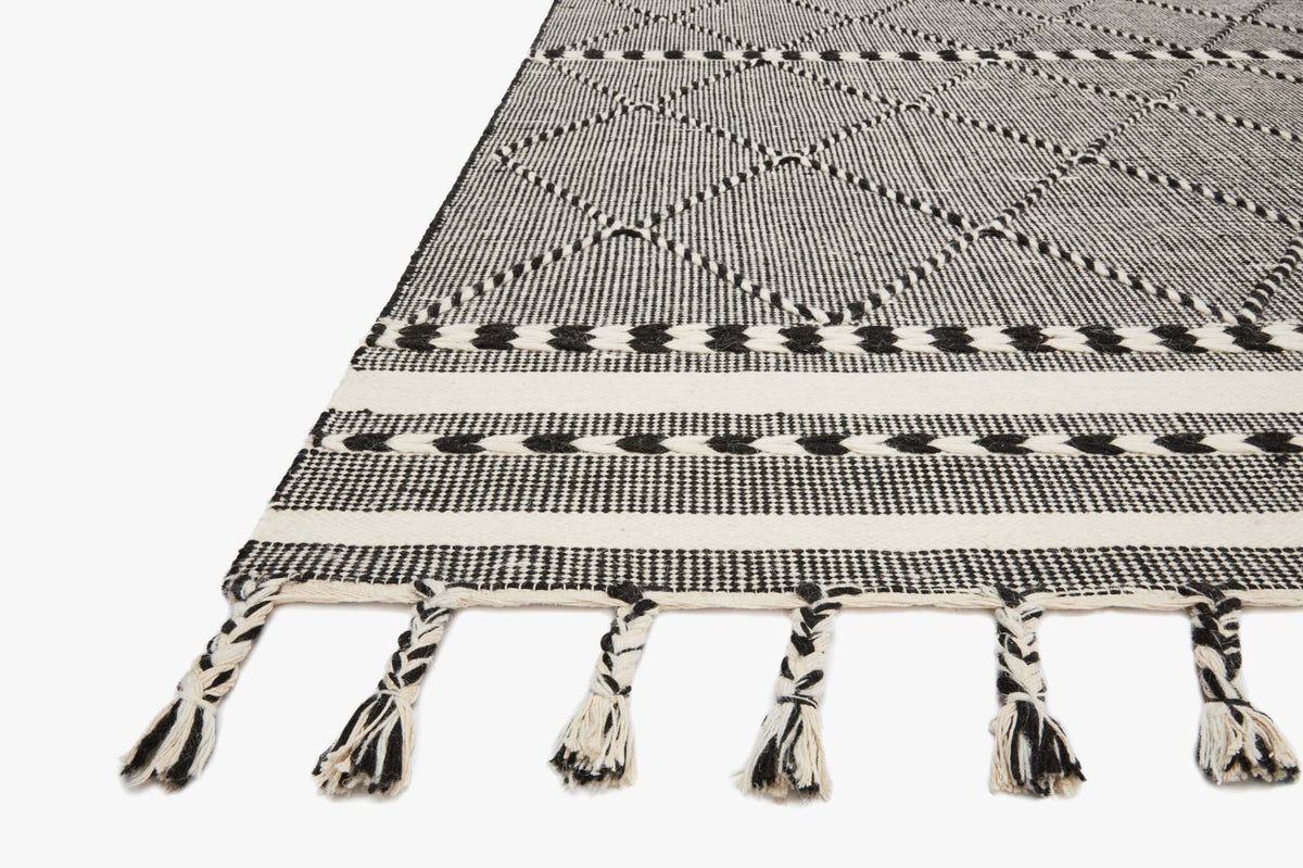 Corner view of black-and-gray diamond rug with striped border and hanging tassels