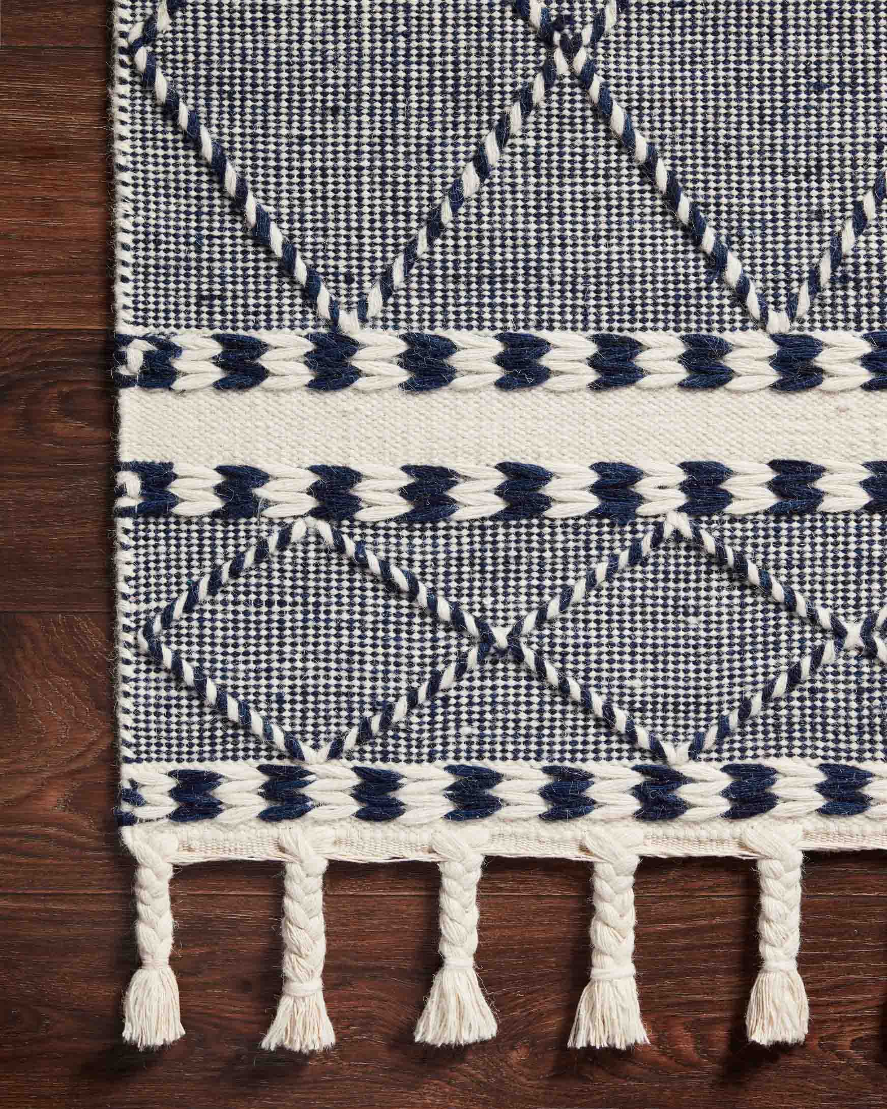 Rug corner with navy and off-white diamond pattern, braided trim, and tasseled fringe
