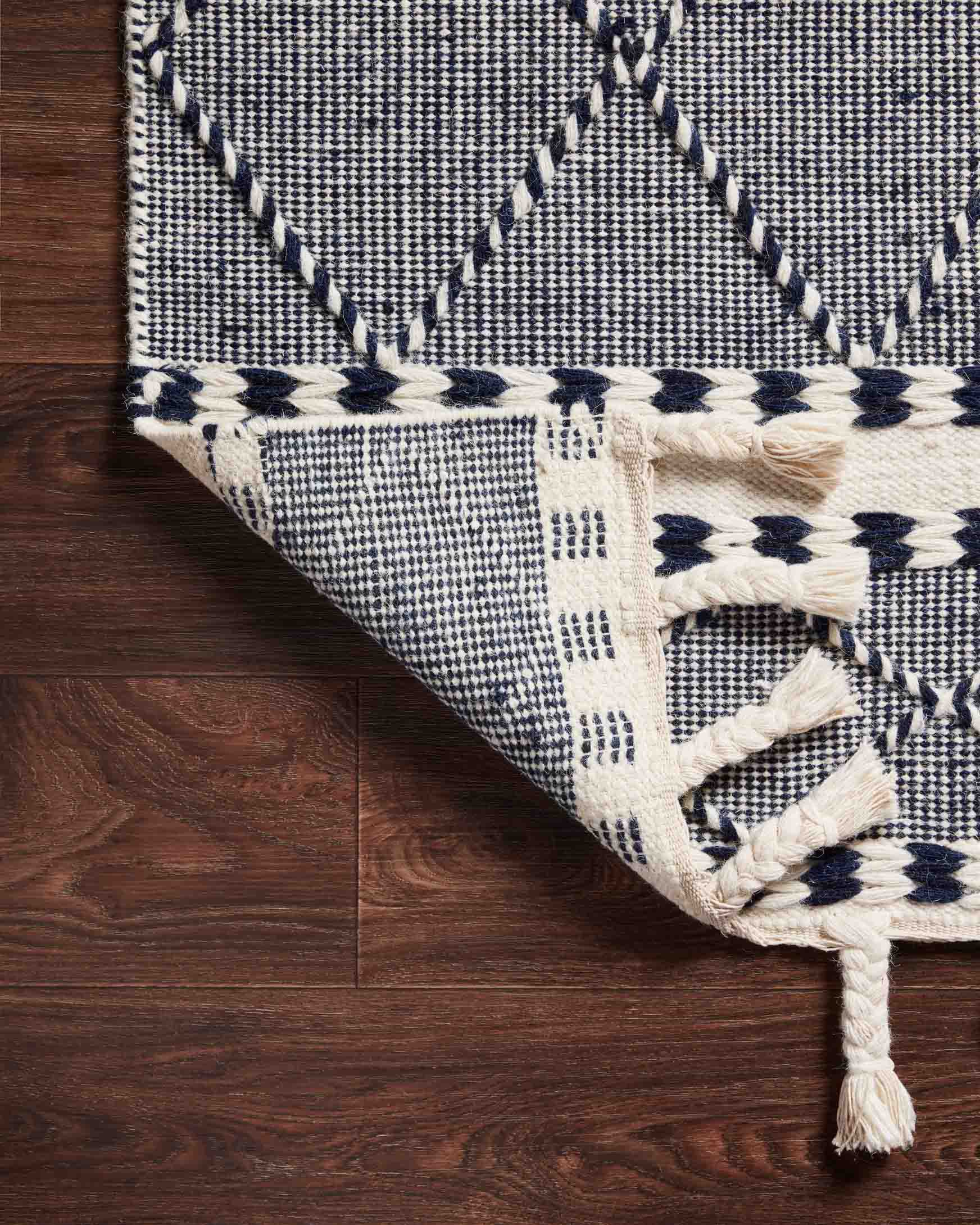 Rug corner detail in navy and off-white with braided border and long fringe