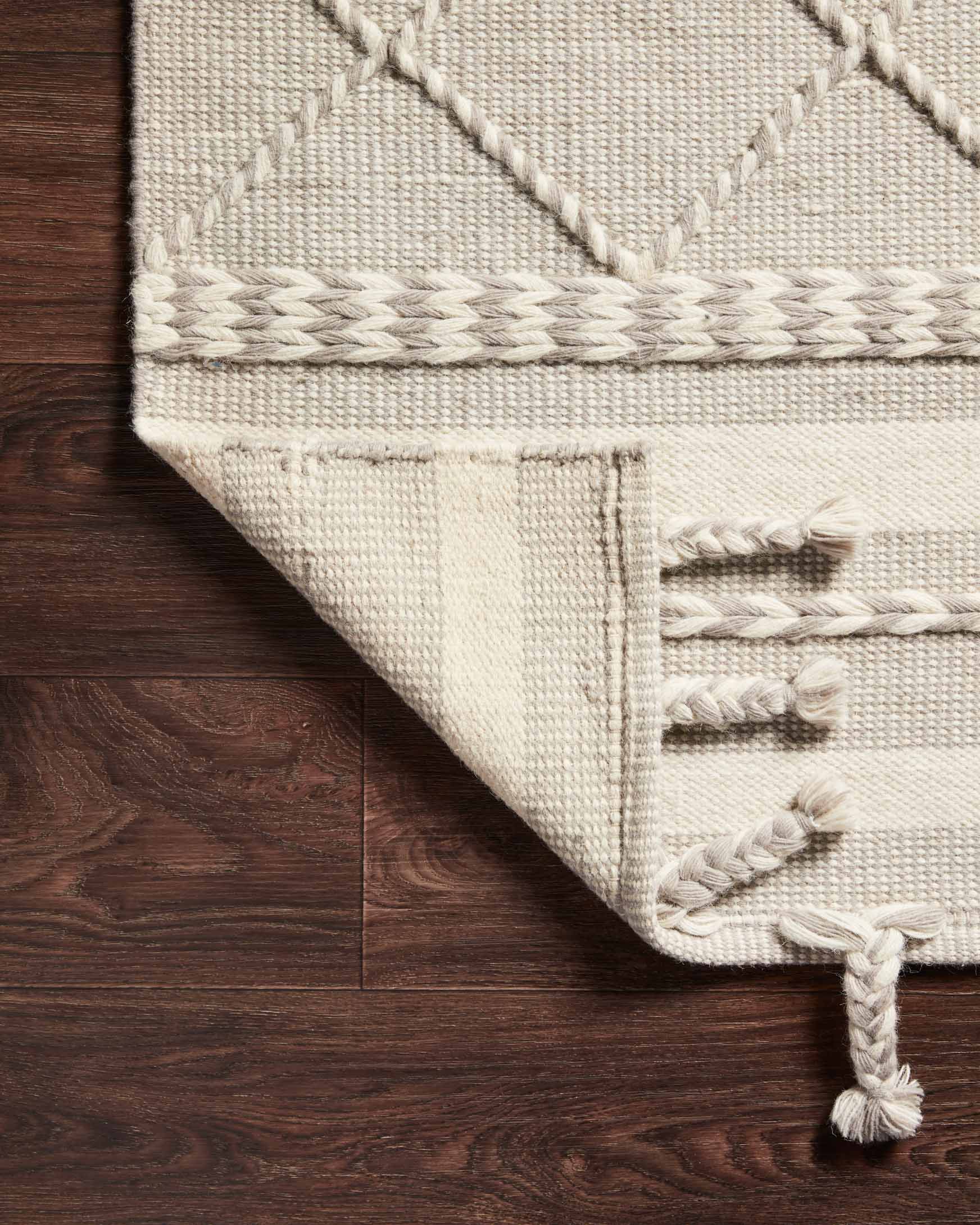 Close-up corner of silver rug with diamond weave, braided edge trim, and tassels