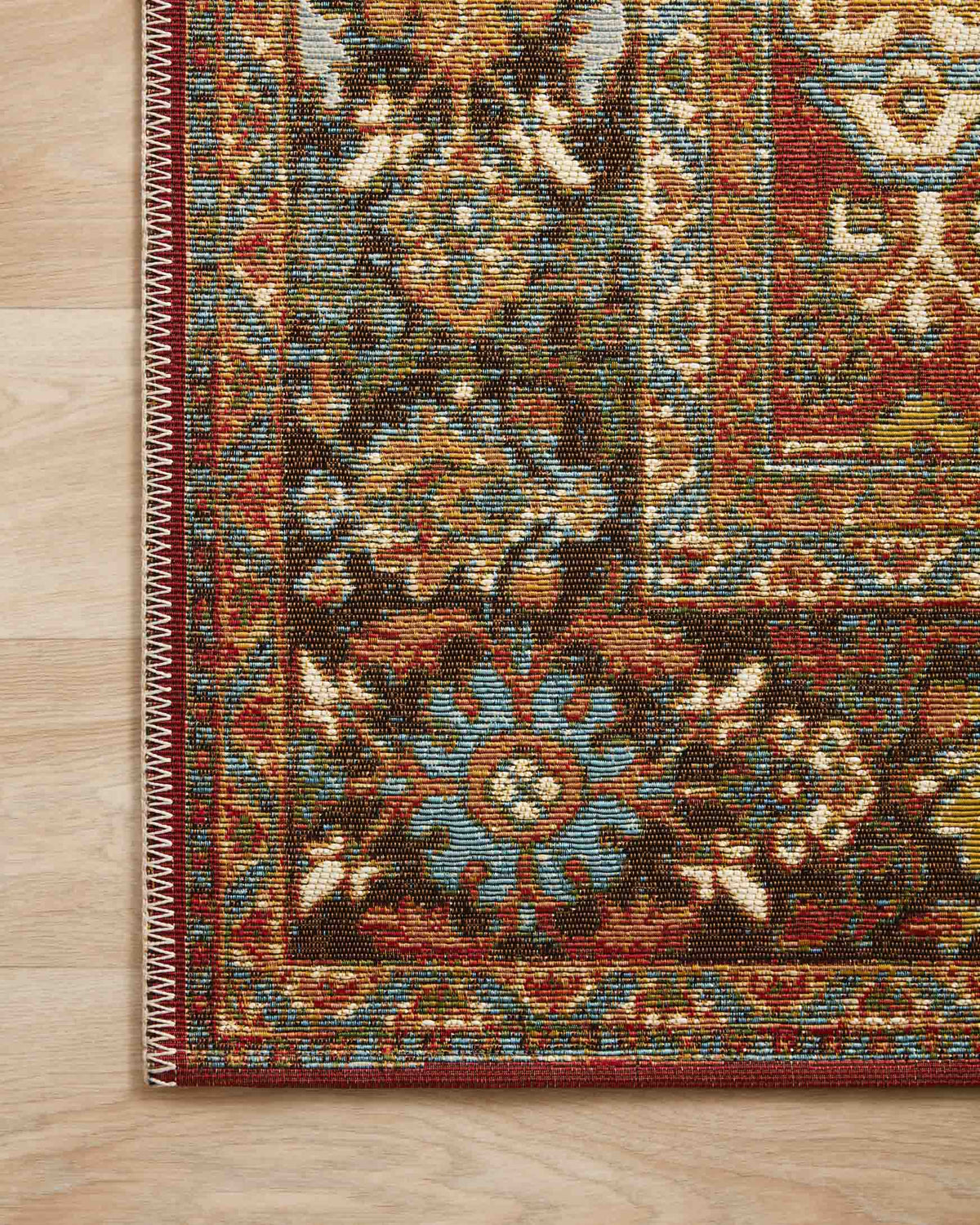 Close-up of red, teal, and gold rug border with dense floral pattern and knot texture