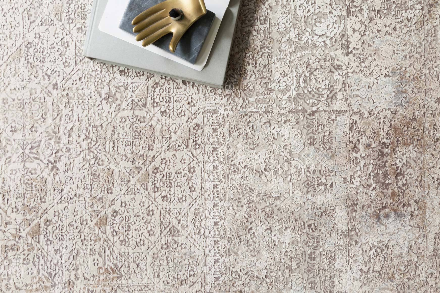 Ivory and pebble power-loomed rug detail with ornate distressed motif texture