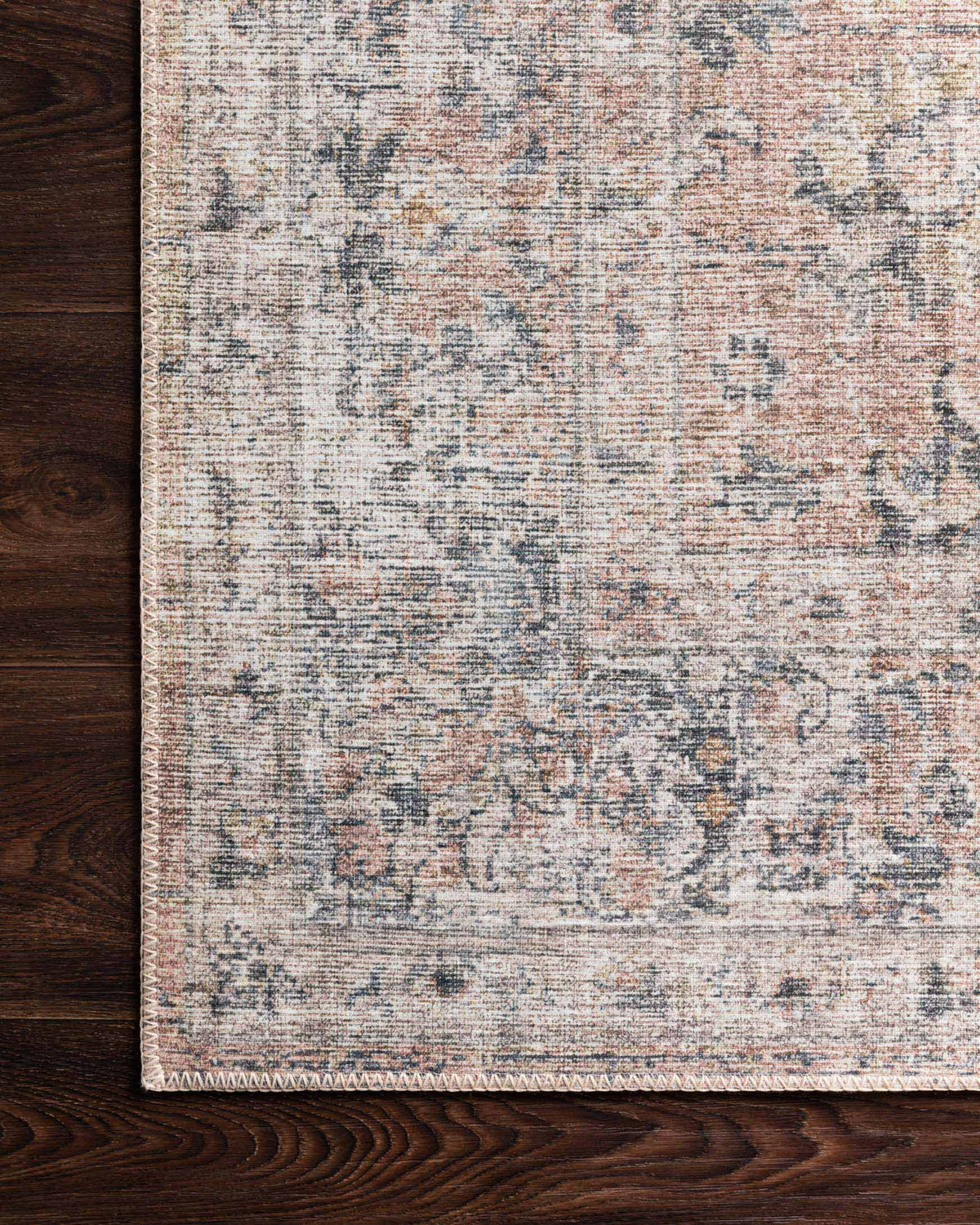 Blush and grey rug corner with distressed pattern on dark wooden floor.