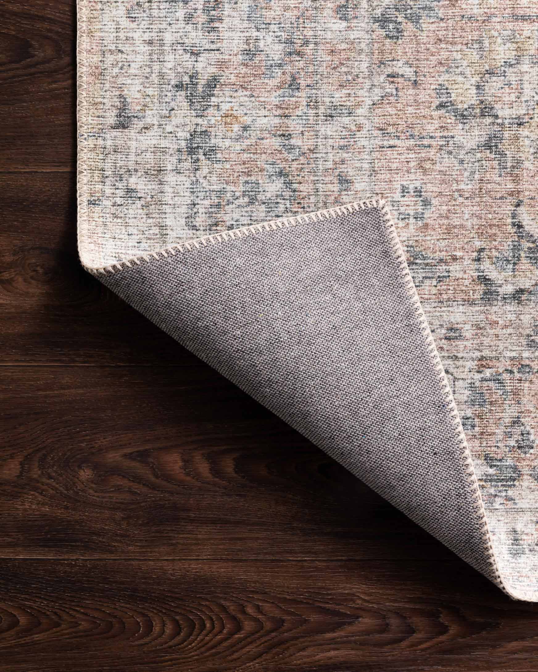 Blush and grey rug edge with stitched border and distressed pattern on wood floor.