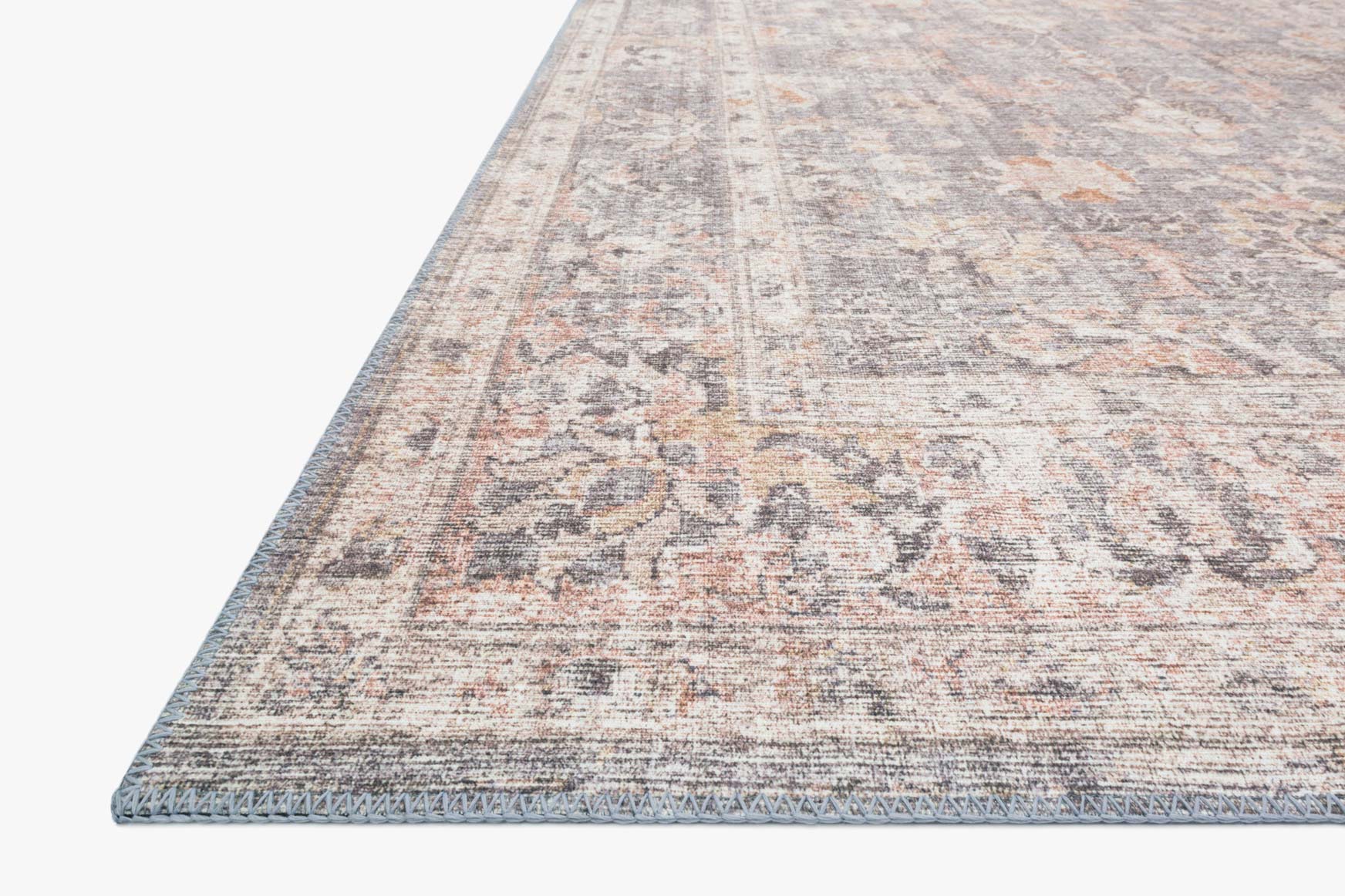 Close-up corner of grey and apricot distressed rug with ornate medallion motifs.