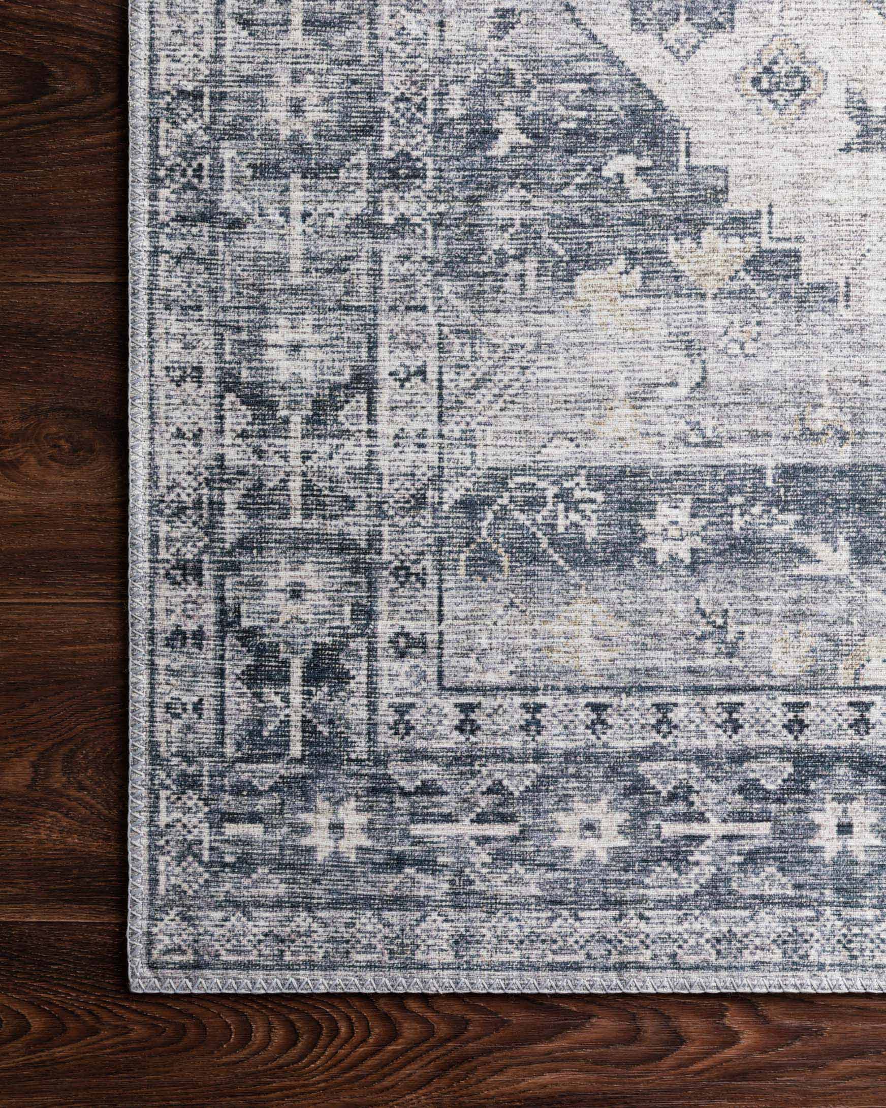Close-up of silver and grey rug surface with geometric blocks and patterned edge.