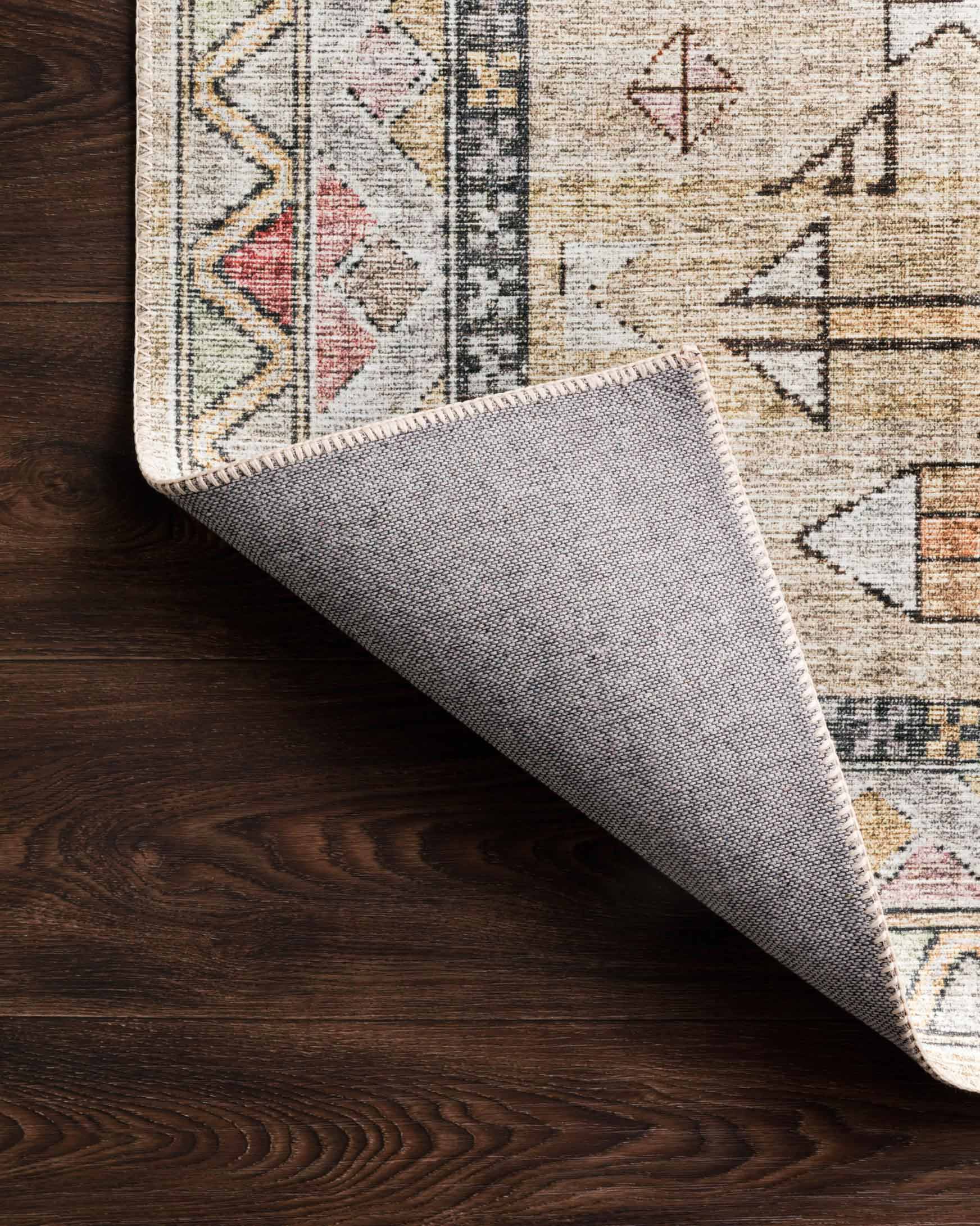 Traditional rug edge rolled on dark wood floor, showing cream base and multicolor pattern