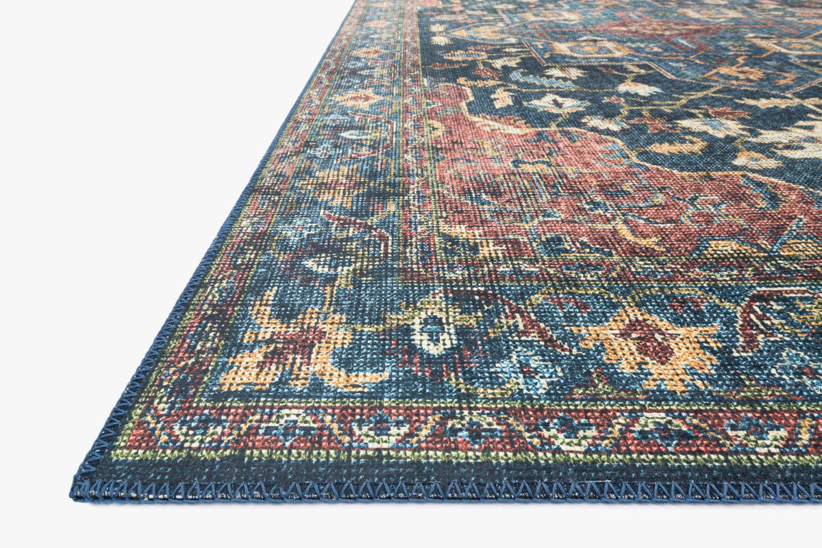 Corner close-up of ornate area rug in denim blue with brick red woven detailing