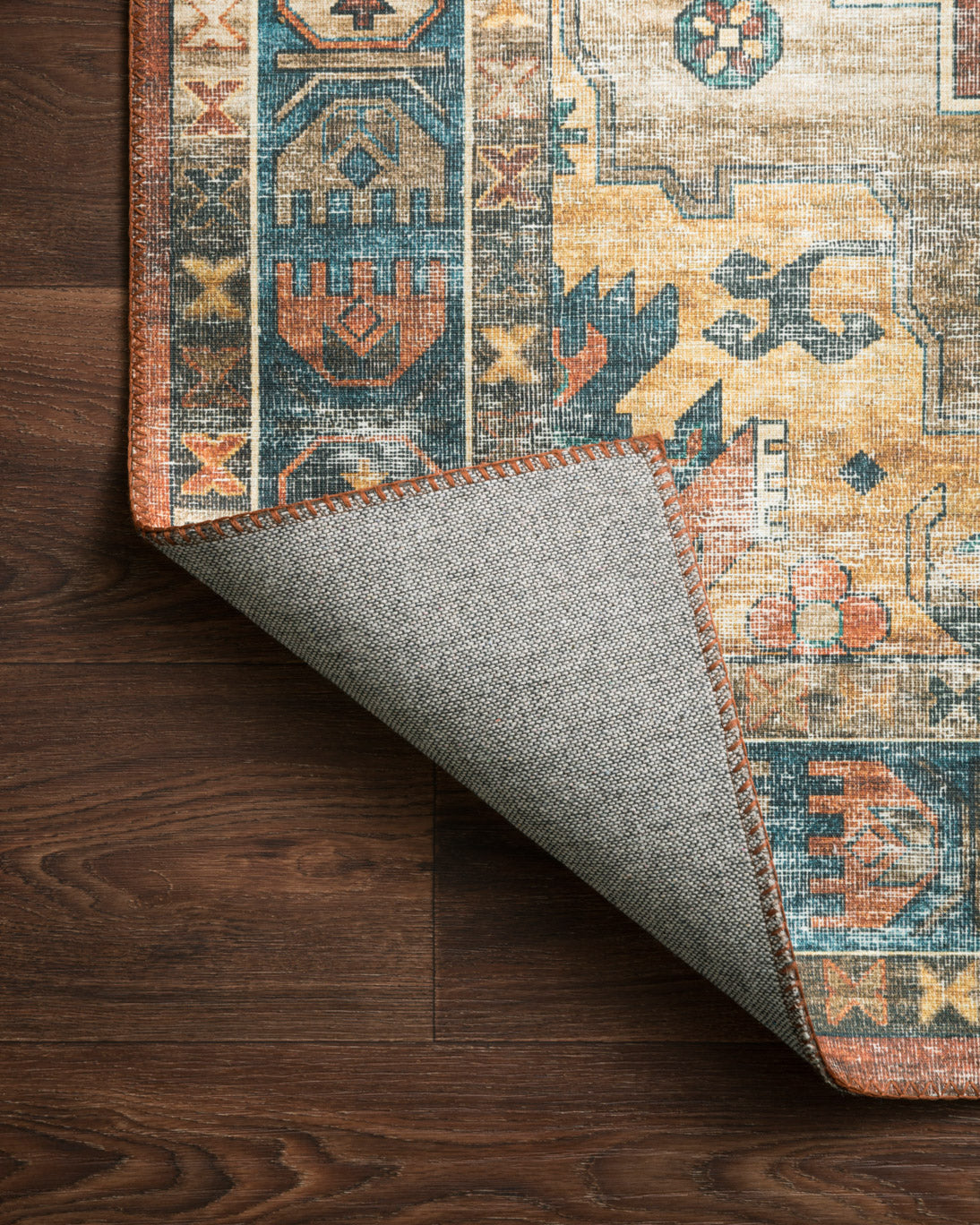 Rust and blue rug corner with light backing fabric and visible stitched edge
