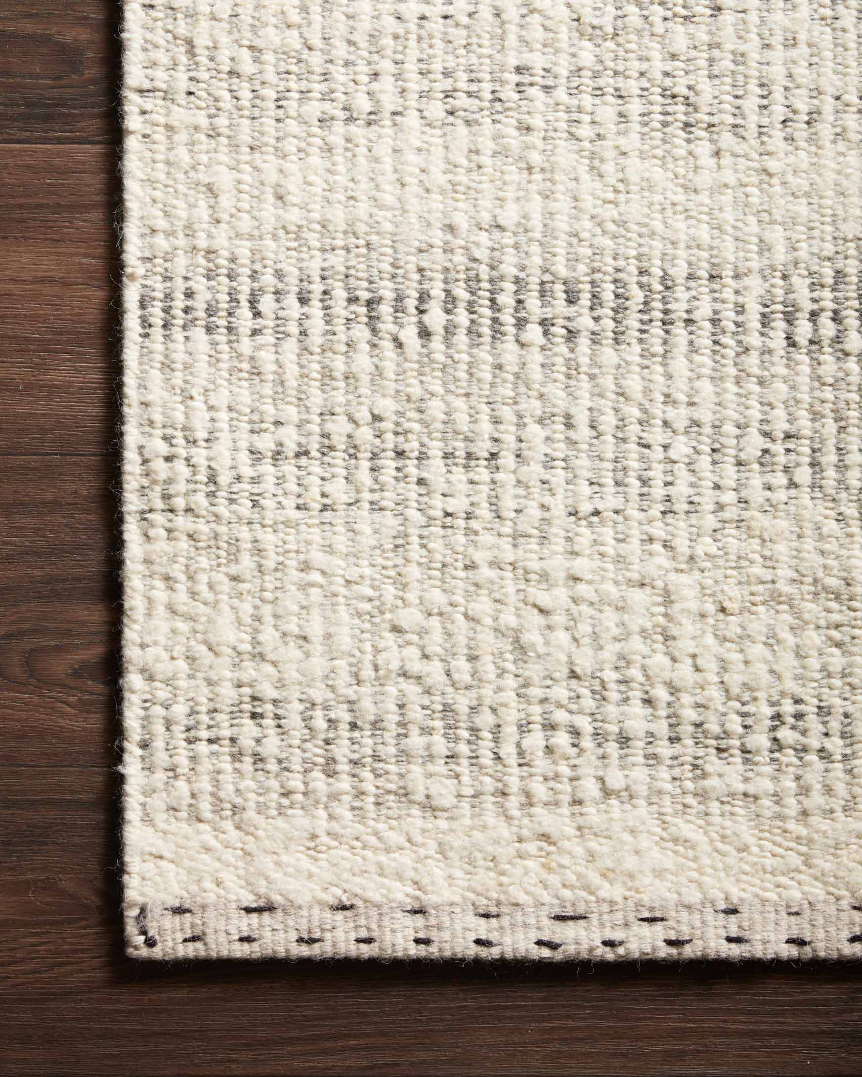 Close-up of cream rug with speckled smoke-gray weave and black edge stitching