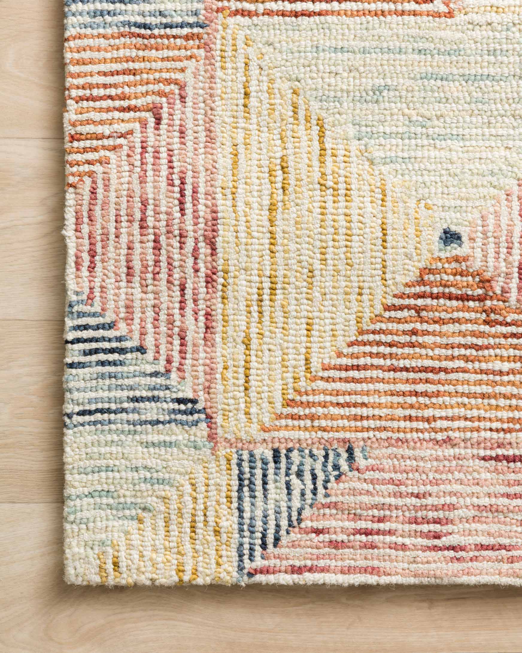 Hooked rug texture and border detail in ivory with coral, blue, and pale yellow pattern