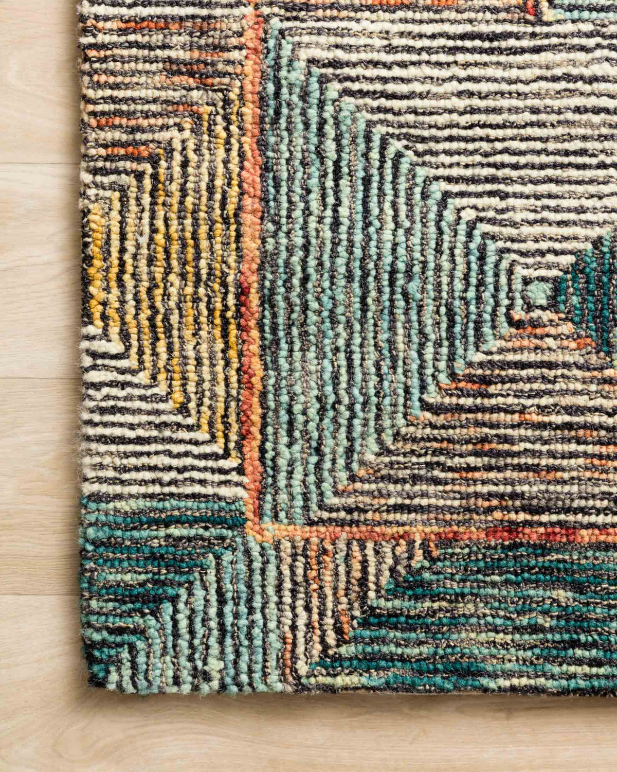 Close-up corner of geometric hooked rug with zigzag lines in teal, tan, orange and rust.