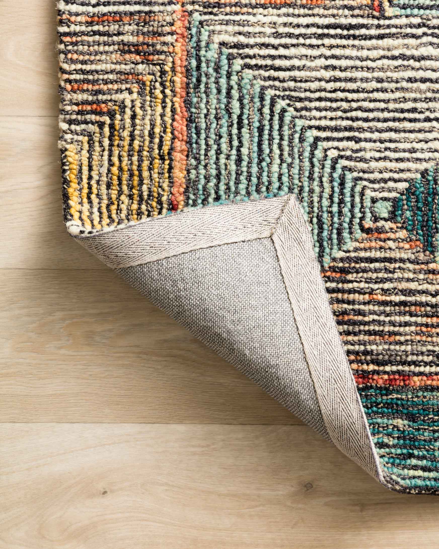 Hooked rug corner with backing visible, multicolor teal and tan geometric pattern.