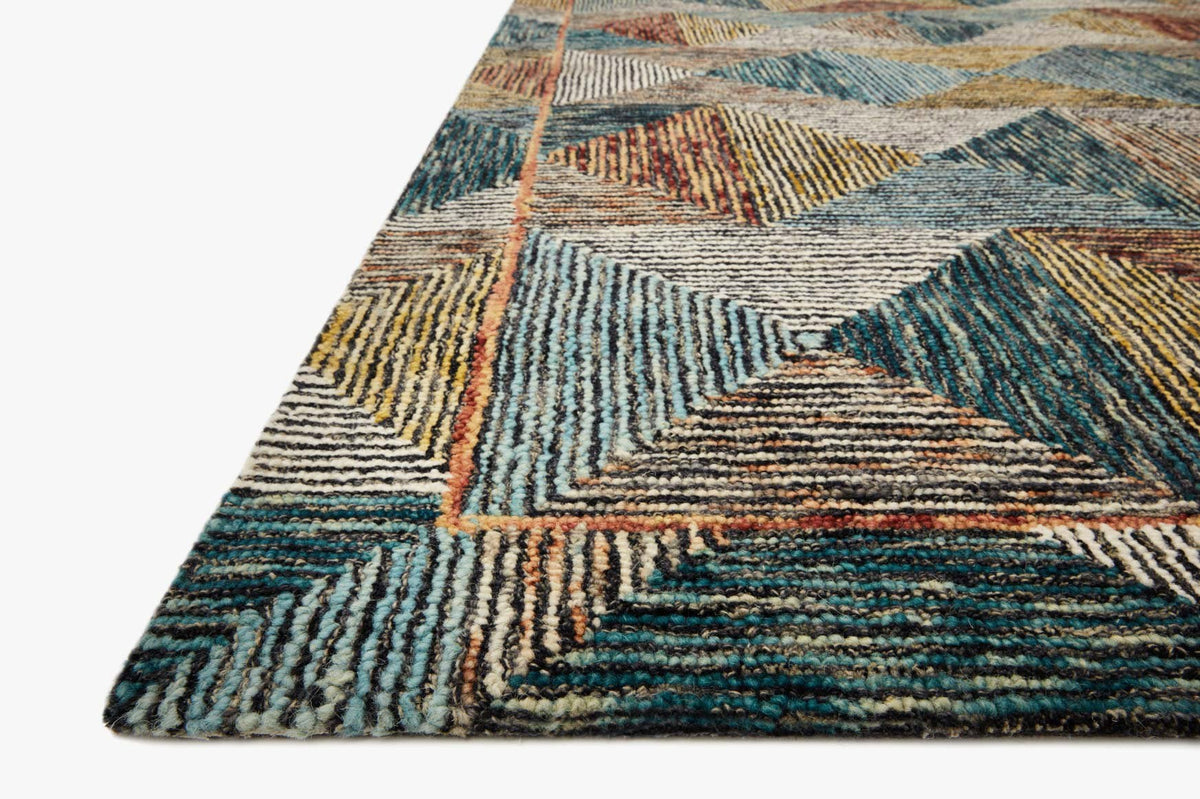 Close-up of geometric hooked rug with textured chevrons in teal, tan, and rust borders.