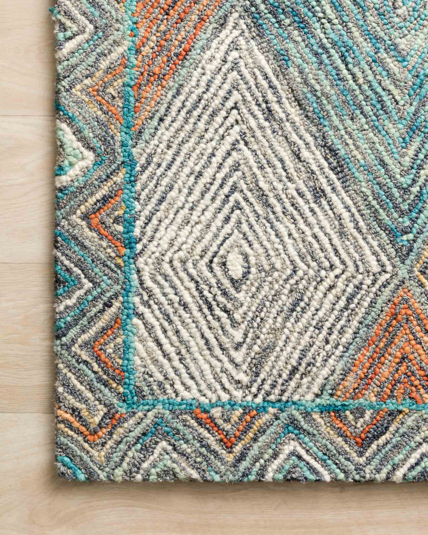 Detail of hooked rug edge with teal and orange border and dense cream diamond center