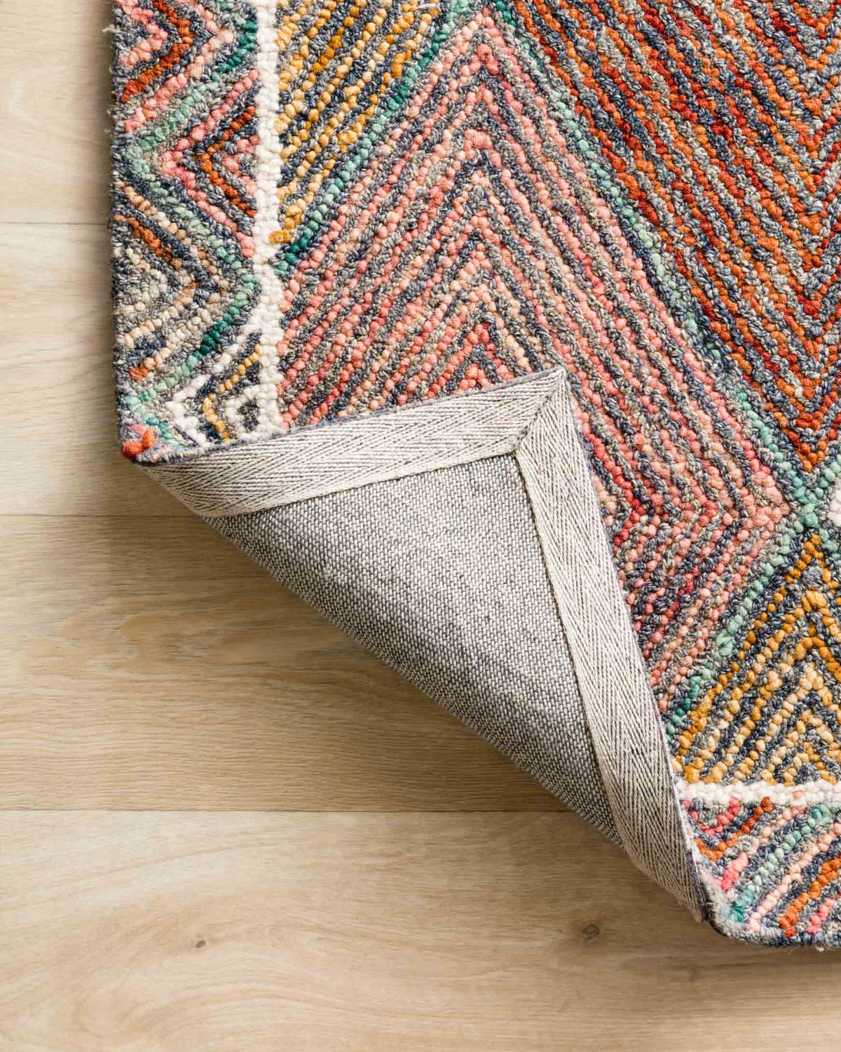 Edge view of hooked rug showing multicolor pile and woven beige backing underside